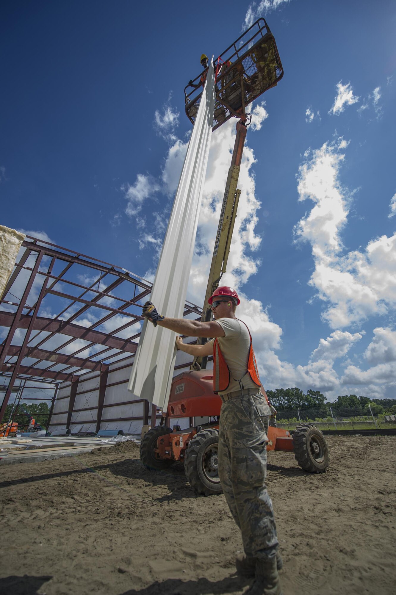 (on the ground) Senior Airman Bradley Schipper, 556th RHS at Hurlburt Field, Florida, and (On the articulating boom lift) Senior Airman Darrien Anderson, 560th RED HORSE Squadron at Joint Base Charleston, S.C., move a piece of siding before attaching it to the steel frame of a building during a construction project at Joint Base Charleston.  Members of the 560th RHS, 628th Civil Engineer Squadron at Joint Base Charleston, 556th RHS, 555th RHS from Nellis Air Force Base, Nevada, and 567th RHS from Seymour Johnson Air Force Base, North Carolina joined forces June, July and August at Joint Base Charleston to build a 4,800 square-foot preengineered  building building to store 560th RHS construction equipment and gear.  Rapid Engineer Deployable, Heavy Operational Repair Squadron, Engineer (RED HORSE) squadrons provide the Air Force with a highly mobile civil engineering capability in support of contingency and special operations worldwide. They are self-sufficient, mobile squadrons that provide heavy construction support such as runway/facility construction, electrical upgrades, and equipment transport when requirements exceed normal base civil engineer capabilities and where Army engineer support is not readily available. (U.S. Air Force Photo by Michael Dukes)