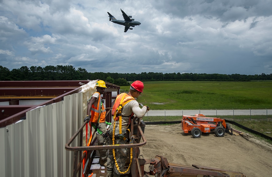 A Charleston C-17 Globemaster III approaches to land while members of the 560th RED HORSE Squadron and the 628th Civil Engineer Squadron at Joint Base Charleston, Sout Carolina and the 555th RHS from Nellis Air Force Base, Nevada, and the 567th RHS from Seymour Johnson Air Force Base, North Carolina joined forces at Joint Base Charleston to build a 4,800 square-foot preengineered  building building to store construction equipment and gear.  Rapid Engineer Deployable, Heavy Operational Repair Squadron, Engineer (RED HORSE) squadrons provide the Air Force with a highly mobile civil engineering capability in support of contingency and special operations worldwide. They are self-sufficient, mobile squadrons that provide heavy construction support such as runway/facility construction, electrical upgrades, and equipment transport when requirements exceed normal base civil engineer capabilities and where Army engineer support is not readily available. (U.S. Air Force Photo by Michael Dukes)