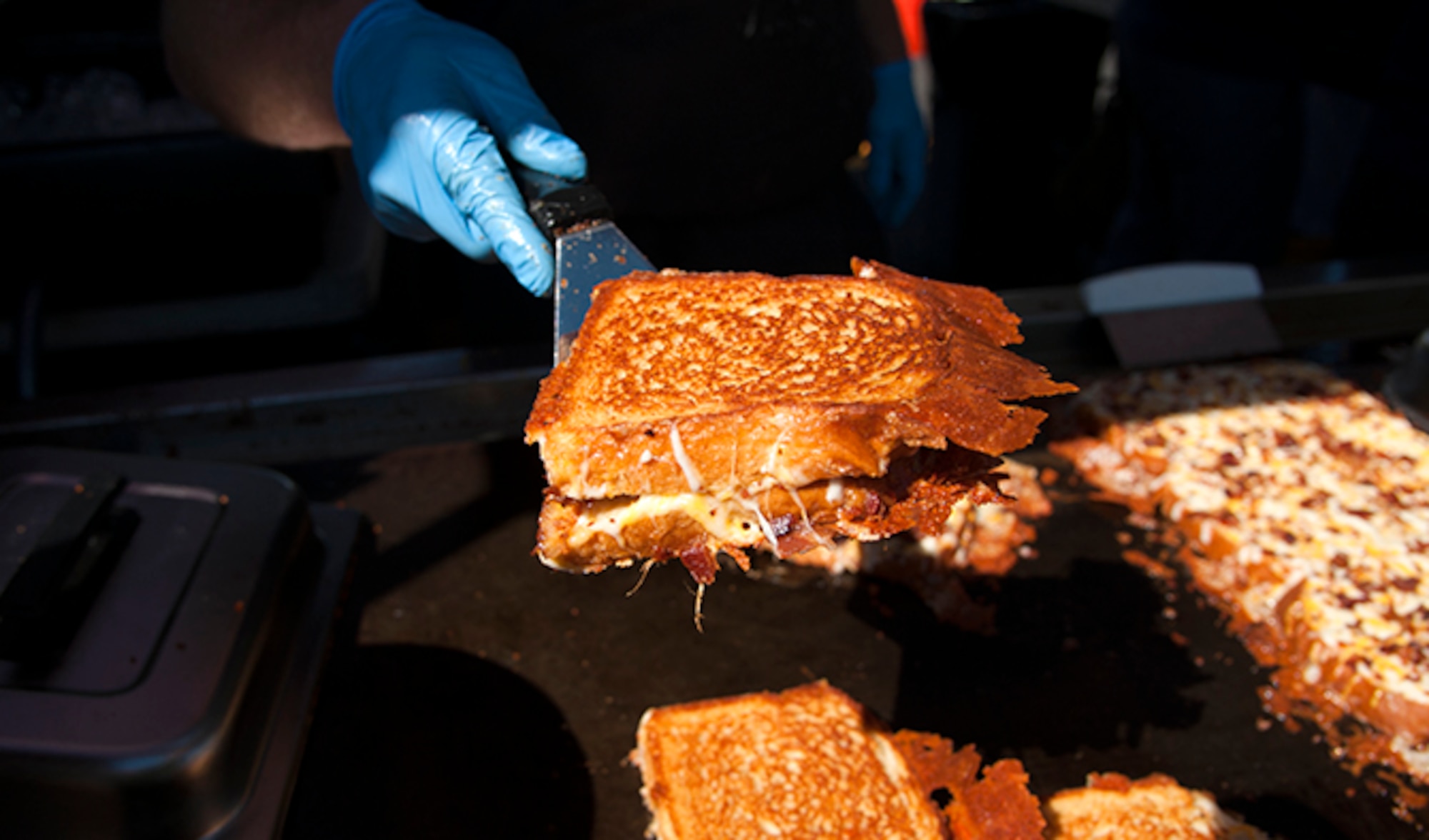 Joe McCarthy, the owner of Meltz Extreme Grilled Cheese, offers up a grilled bacon and cheese sandwich during the Food Truck Festival, Aug. 26, 2016, at Fairchild Air Force Base, Wash. Meltz Extreme Grilled Cheese was one of 10 food trucks to offer free menu samples to all attendees.  (U.S. Air Force photo/Airman 1st Class Ryan Lackey)
