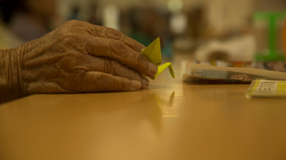 An elderly women holds a crane given to her by Staff Sgt. Ismael Esconde at a nursing home in Kin, Okinawa on Nov. 25, 2016. Esconde wanted to make a difference during his six-month unit deployment program to Okinawa, Japan with Headquarters and Service Company, 3rd Battalion, 3rd Marine Regiment as the substance abuse control officer. He heard about the Legend of 1,000 Cranes and thought it would be a good way to show respect to the hospitals and nursing homes to which he gifted them. Esconde is from Los Angeles, California. (U.S. Marine Corps photo by Lance Cpl. Kelsey Dornfeld/Released)