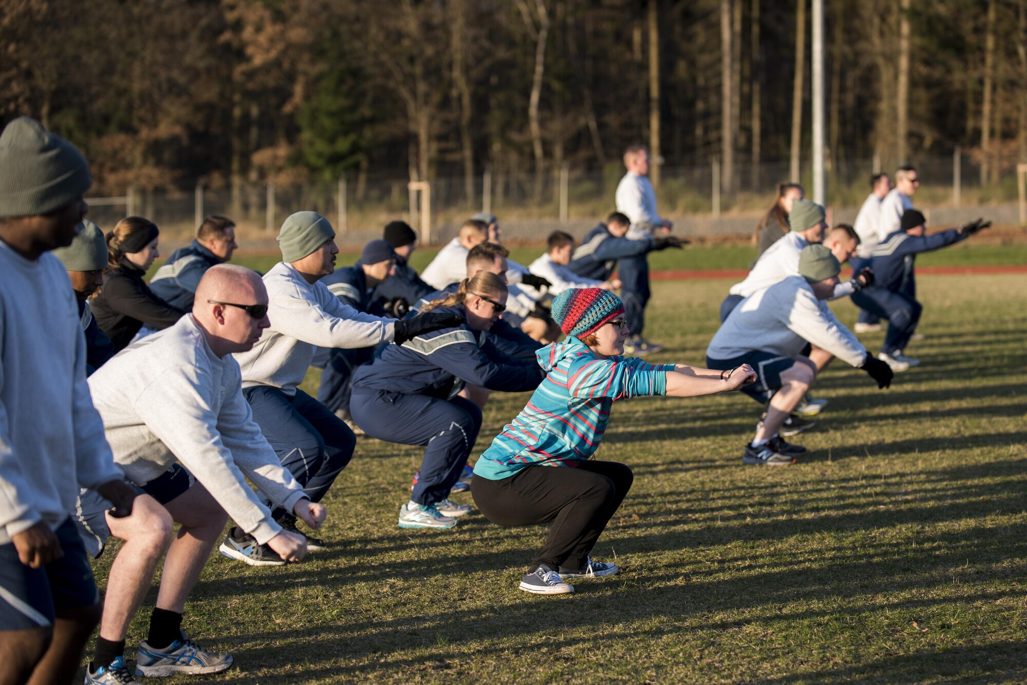 Airmen perform squats during a physical training warm-up outside the Powerehaus Fitness Center track on Spangdahlem Air Base, Germany, Nov. 30, 2016. The warm-up was held before beginning an exercise routine with the new Fitness-In-A-Box, a lockable unit complete with strength and conditioning training equipment. (U.S. Air Force photo by Airman 1st Class Preston Cherry)
