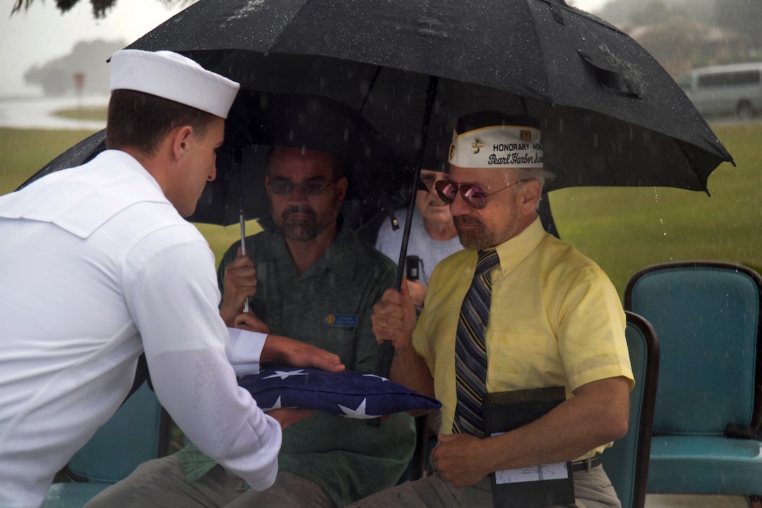 A member of the Joint Base Pearl Harbor-Hickam honors and ceremonial guard presents Bob Bracci, honorary member of the Pearl Harbor Survivors Association, with an ensign during an ash-scattering ceremony at the USS Utah Memorial, Dec. 1, 2016. Ashes were scattered of Jack A. Stoeber, a Pearl Harbor attacks survivor who recently passed away. Navy photo by Petty Officer 2nd Class Gabrielle Joyner