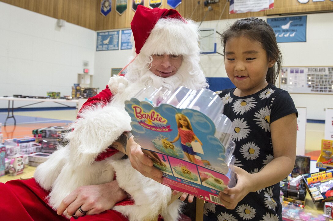 A little girl receives a Barbie doll from Santa Claus during Toys for Tots at Nunachiam Sissauni School in Buckland, Alaska, Nov. 29, 2016. Santa was assisted by by Marine Corps 1st Sgt. Joshua Guffey, the inspector-instructor first sergeant assigned to Detachment Delta, 4th Law Enforcement Battalion. Air Force photo by Alejandro Pena