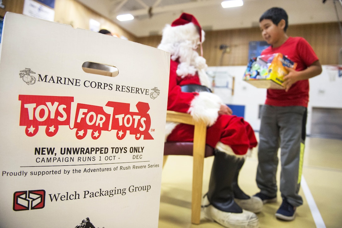 Santa Claus hands out presents to children during Toys for Tots at Nunachiam Sissauni School in Buckland, Alaska, Nov. 29, 2016. Santa was assisted by by Marine Corps 1st Sgt. Joshua Guffey, the inspector-instructor first sergeant assigned to Detachment Delta, 4th Law Enforcement Battalion. Air Force photo by Alejandro Pena