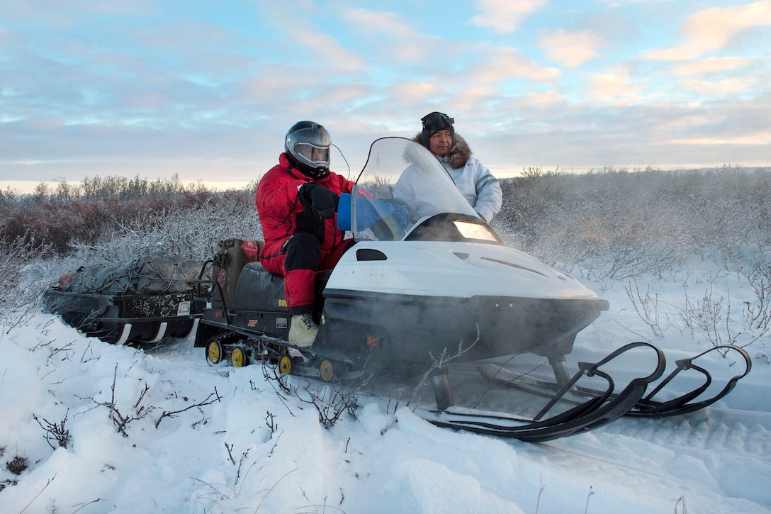 Marine Corps Capt. Michael Sickels, left, talks with Dickie Moto, a local guide, while traveling via snow machine from Buckland to Deering, Alaska, Nov. 29, 2016. Sickels, an inspector-instructor assigned to Detachment Delta, 4th Law Enforcement Battalion, and Moto traveled to Deering to deliver gifts for Alaskan children while participating in Toys for Tots. Air Force photo by Alejandro Pena
