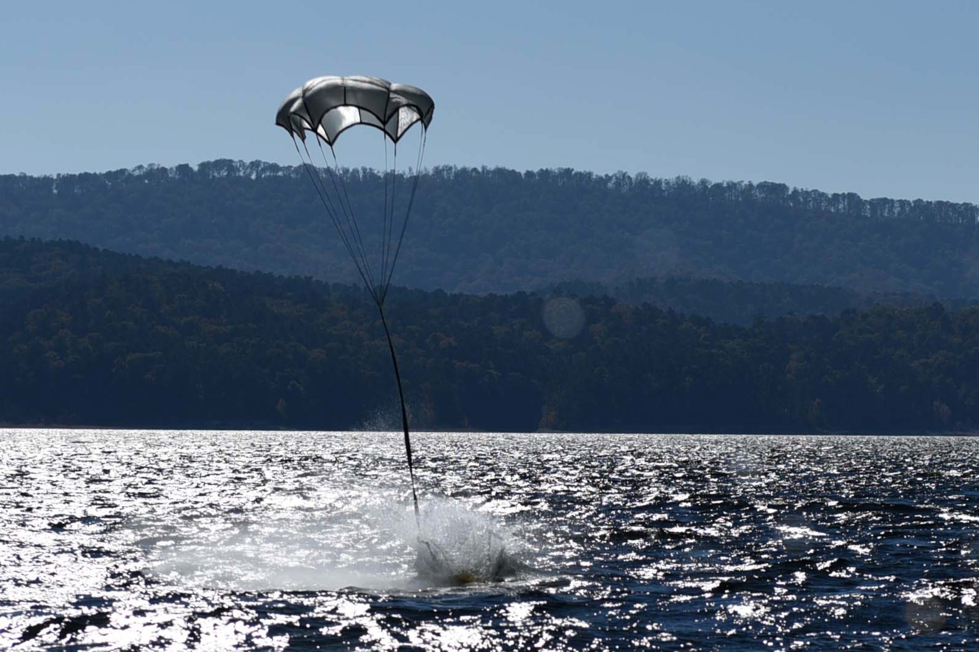 A pelican case drops from a C-130J and lands on the water during a search and rescue exercise as part of a Turkey Shoot competition Nov. 17, 2016, at Lake Ouachita, Ark. The pelican case was filled with metal plates weighing 31 pounds to simulate food and medical supplies. (U.S. Air Force photo by Airman 1st Class Kevin Sommer Giron)