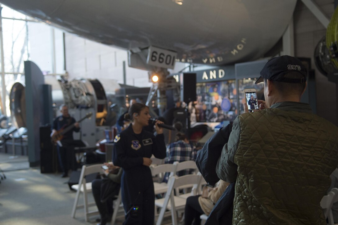 A man takes a photo of Tech. Sgt. Nalani Quintello, Max Impact lead vocalist, as she performs at the Smithsonian National Air and Space Museum in Washington, D.C., Dec. 2, 2016. The band performed several times throughout the afternoon, playing several holiday favorites. (U.S. Air Force photo by Senior Airman Mariah Haddenham)
