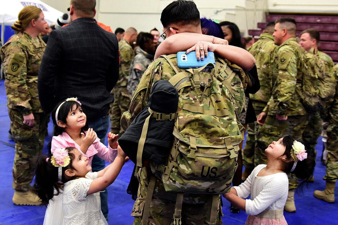 Army Spc. Christopher Kelley embraces his wife, Lydia Kelley, while his daughters Kairi, 4, Trinity, 3, and Aurora, 6, wait to hug him after a welcome home ceremony at the Buckner Physical Fitness Center, Joint Base Elmendorf-Richardson, Alaska, Dec. 1, 2016. Kelley is assigned to the 109th Transportation Company, 17th Combat Sustainment Support Battalion, and was returning from a deployment to Kuwait. Army photo by John Pennell