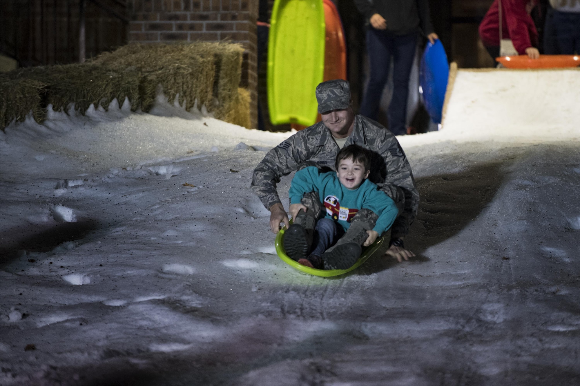 Staff Sgt. Joshua Humes, 23d Civil Engineer Squadron fire protection crew chief, and his son, Brody, sled down a slope after a tree-lighting ceremony, Dec. 2, 2016, at Moody Air Force Base, Ga. Two separate snow areas were created for children to play and sled. (U.S. Air Force photo by Airman 1st Class Daniel Snider)