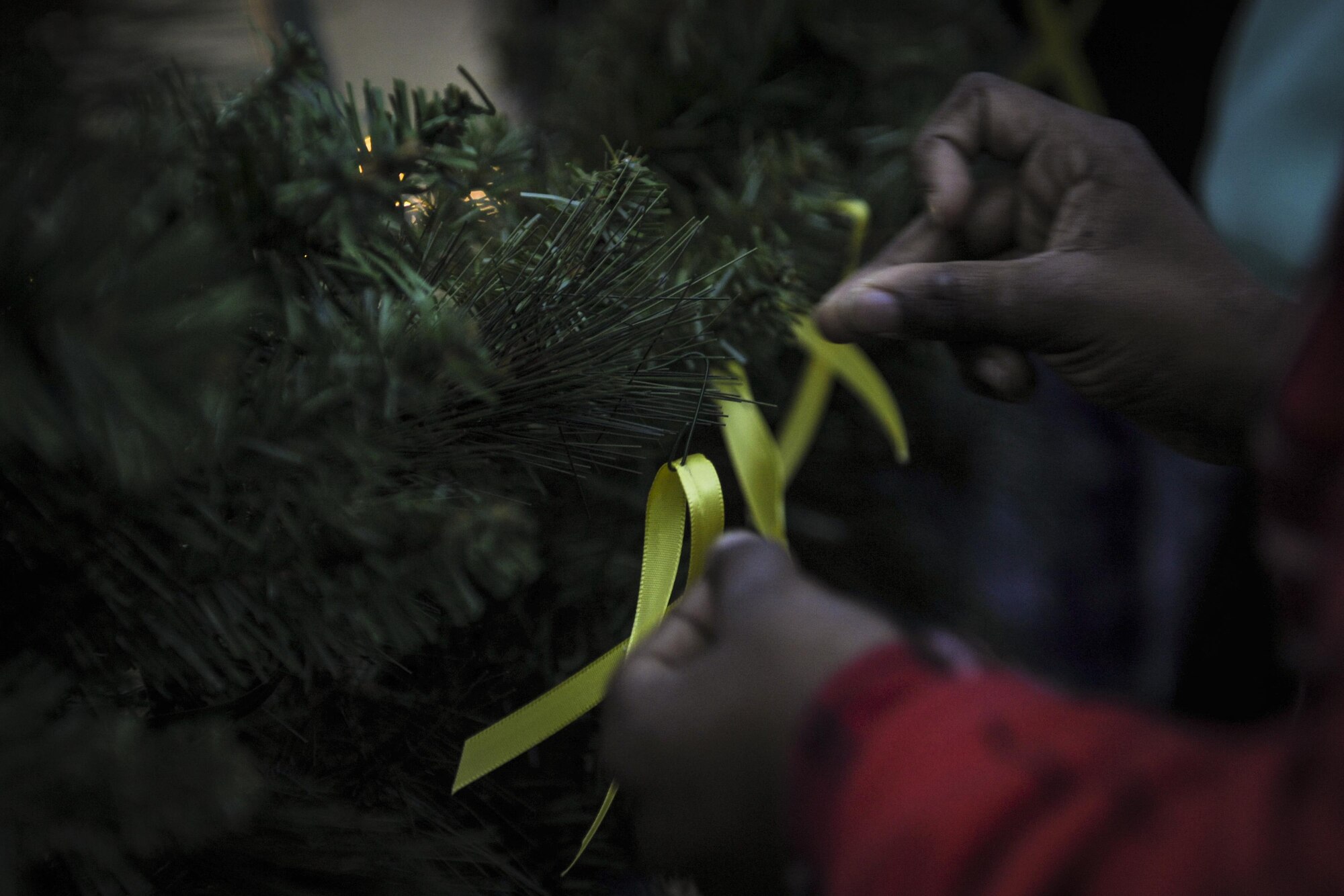 Family members pin yellow ribbons on a wreath during the Christmas tree lighting ceremony at Hurlburt Field, Fla., Dec. 2, 2016. The yellow ribbon is pinned to honor and remember those who are deployed during the holiday season. (U.S. Air Force photo by Airman Dennis Spain)