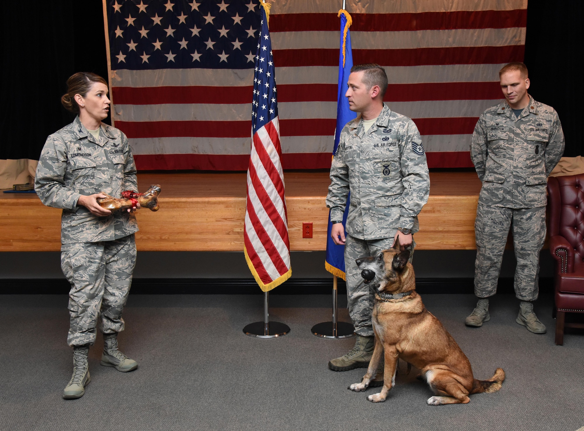 Col. Michele Edmondson, 81st Training Wing commander, delivers remarks to Tech. Sgt. James Martin III, 81st Security Forces Squadron charlie flight flight chief, and Densy, 81st SFS military working dog, during Densy’s retirement ceremony at the Keesler Medical Center Don Wylie Auditorium Dec. 2, 2016, on Keesler Air Force Base, Miss. Densy served more than nine years in the Air Force. After serving together for two years, to include one deployment, Martin adopted Densy. (U.S. Air Force photo by Kemberly Groue)