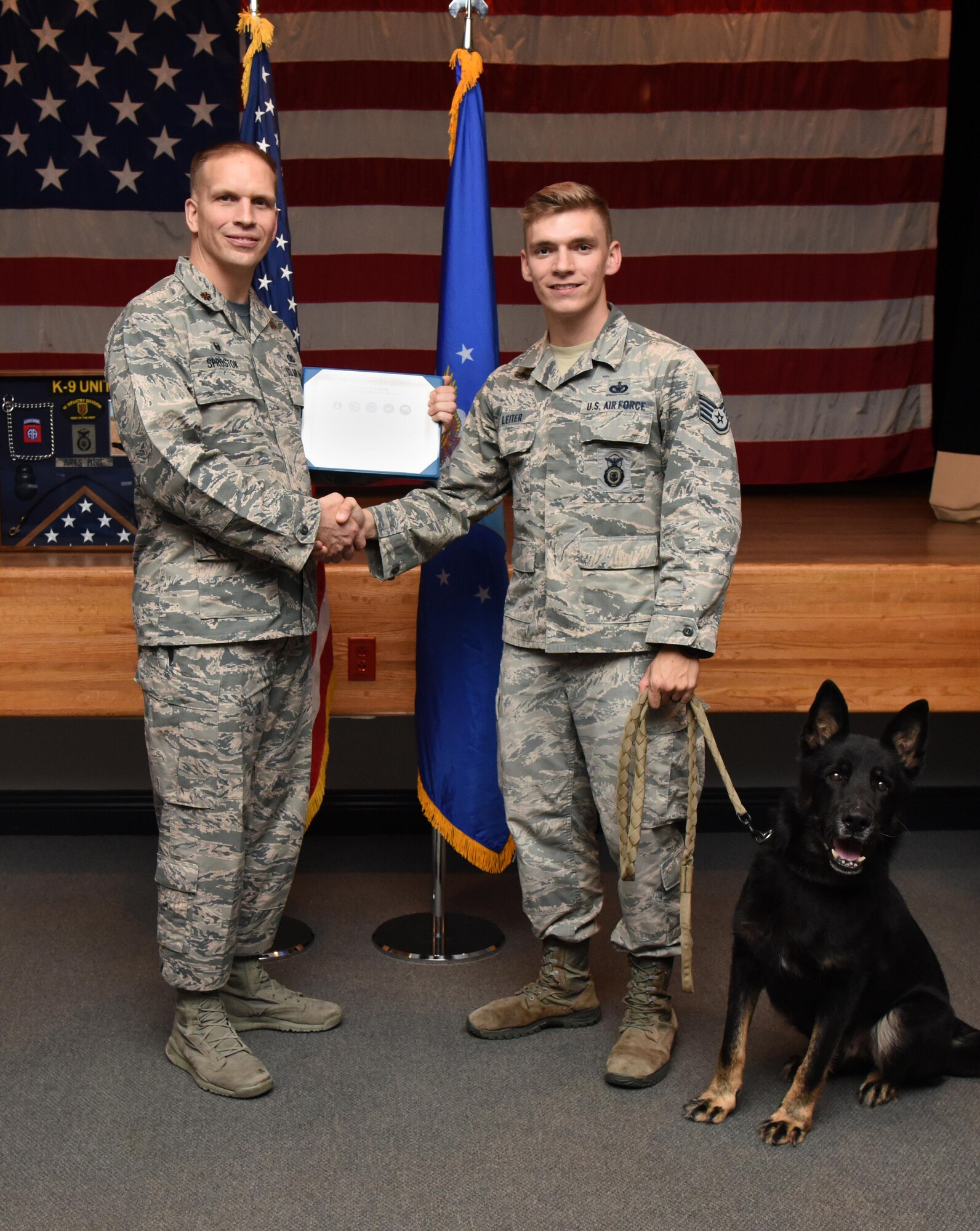 Maj. Devin Sproston, 81st Security Forces Squadron commander, presents a retirement certificate to Staff Sgt. Jordan Leiter, 81st SFS military working dog handler, on behalf of Ares, 81st SFS military working dog, during Ares’s retirement ceremony at the Keesler Medical Center Don Wylie Auditorium Dec. 2, 2016, on Keesler Air Force Base, Miss. He served more than eight years in the Air Force. After serving together for two years, to include one deployment, Leiter adopted Ares. (U.S. Air Force photo by Kemberly Groue)