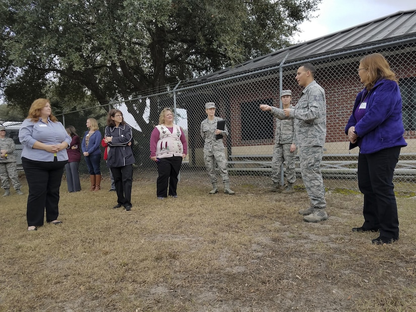Joint Base Charleston spouses listen to Tech. Sgt. Jonathan Calo, 628th Security Forces Squadron military working dog trainer, right, as they participate in a base tour of Joint Base Charleston, S.C., Dec. 5, 2016. Spouses had the opportunity to tour various mission sets across the Air Base.