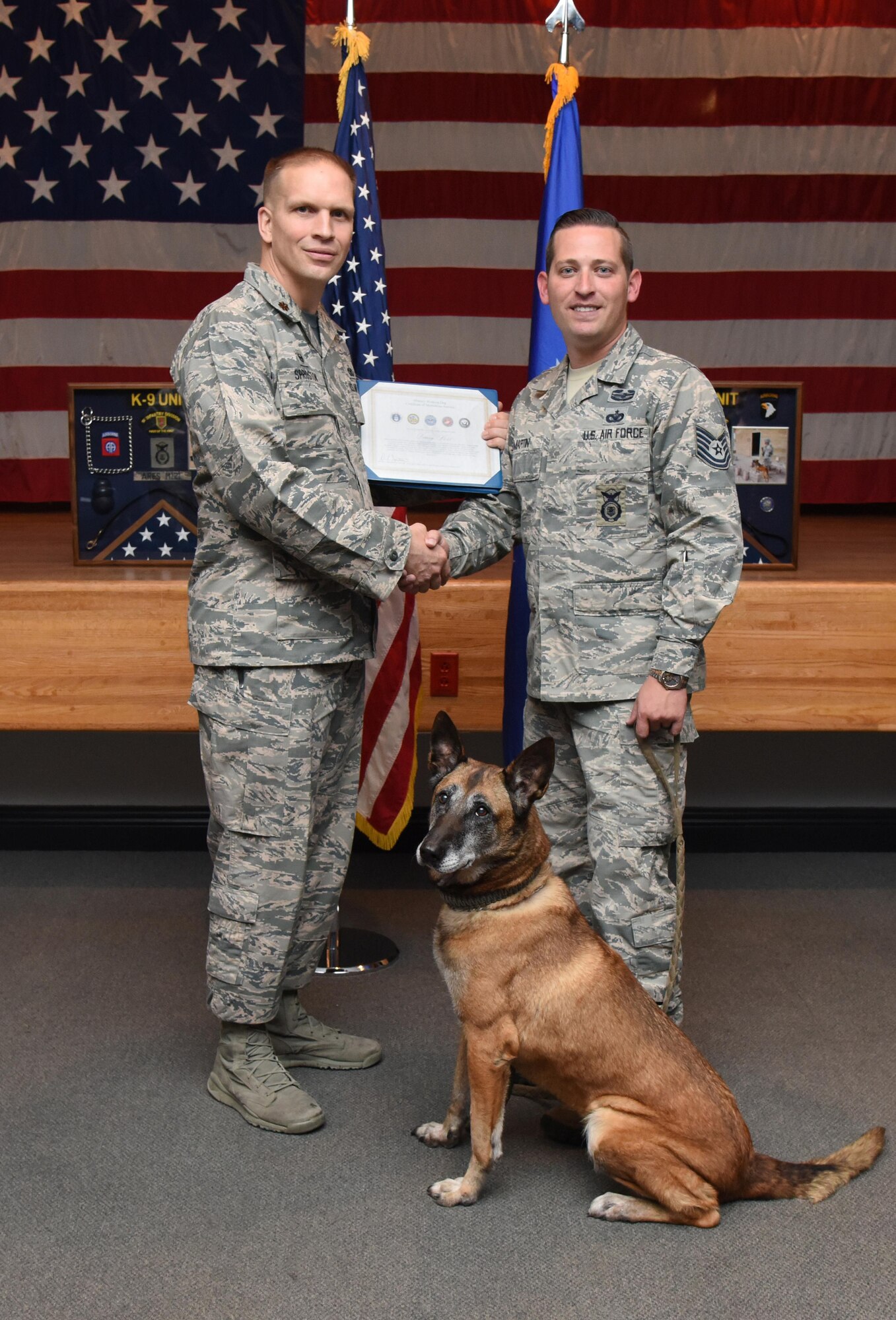 Maj. Devin Sproston, 81st Security Forces Squadron commander, presents a retirement certificate to Tech. Sgt. James Martin III, 81st SFS charlie flight flight chief, on behalf of Densy, 81st SFS military working dog, during Densy’s retirement ceremony at the Keesler Medical Center Don Wylie Auditorium Dec. 2, 2016, on Keesler Air Force Base, Miss. Densy served more than nine years in the Air Force. After serving together for two years, to include one deployment, Martin adopted Densy. (U.S. Air Force photo by Kemberly Groue)
