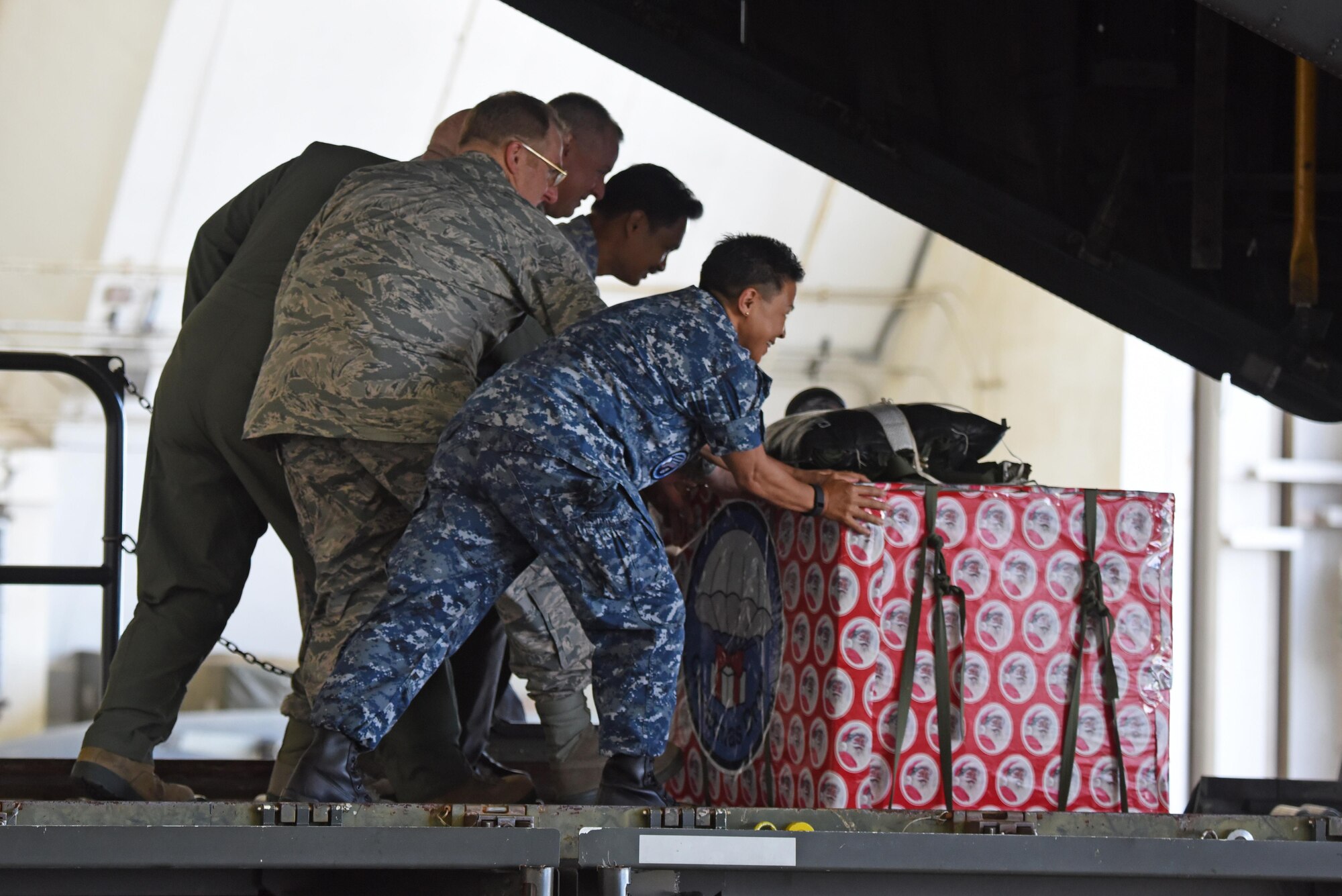 Military and civilian leaders push a box onto a C-130 Hercules during the 2016 Operation Christmas Drop Push Ceremony Dec. 6, 2016, at Andersen Air Force Base, Guam. This year the Japan Air Self-Defense Force, Royal Australian Air Force and U.S. Air Force work together to continue the tradition of air dropping tools, food, clothing and toys throughout the Pacific. (U.S. Air Force Photo by Airman 1st Class Jacob Skovo)