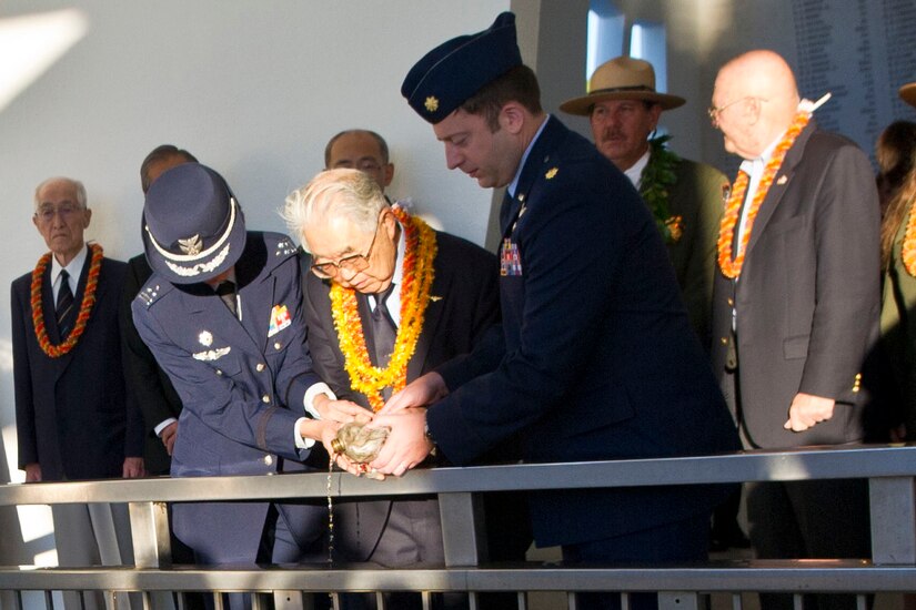 The caretaker of the "Blackened Canteen" tradition, Dr. Hiroya Sugano, center, pours bourbon whiskey into the waters at the USS Arizona Memorial at Pearl Harbor, Hawaii, with a member of the Japanese military, left, and the U.S. Air Force, Dec. 6, 2016. DoD photo by Lisa Ferdinando 