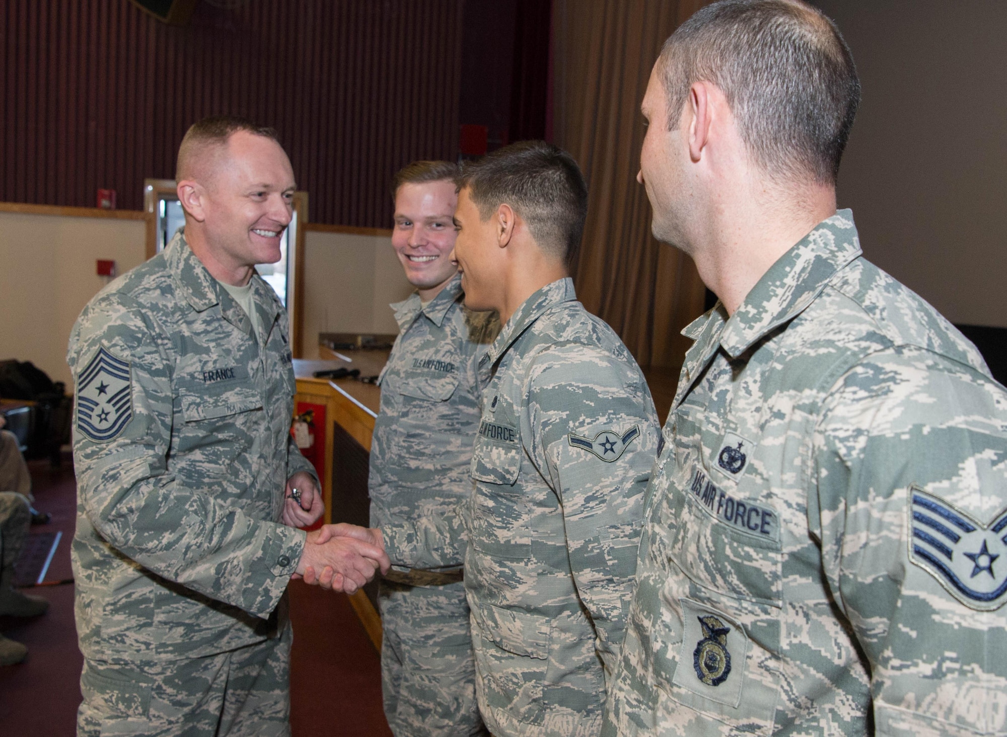 Chief Master Sgt. Jason France, Air Force Materiel Command's command chief, presents a coin to Airman Stephen C. Gary, II, during an enlisted call at the base theater Dec. 1, while Staff Sgt. Richard C. Grathen, right, and Airman 1st Class Steven J. Peplinski, each of whom also received coins, look on. During the enlisted call, France shared his thoughts on a number of topics that affect the command’s enlisted personnel. (U.S. Air Force photo by Jerry Saslav)
