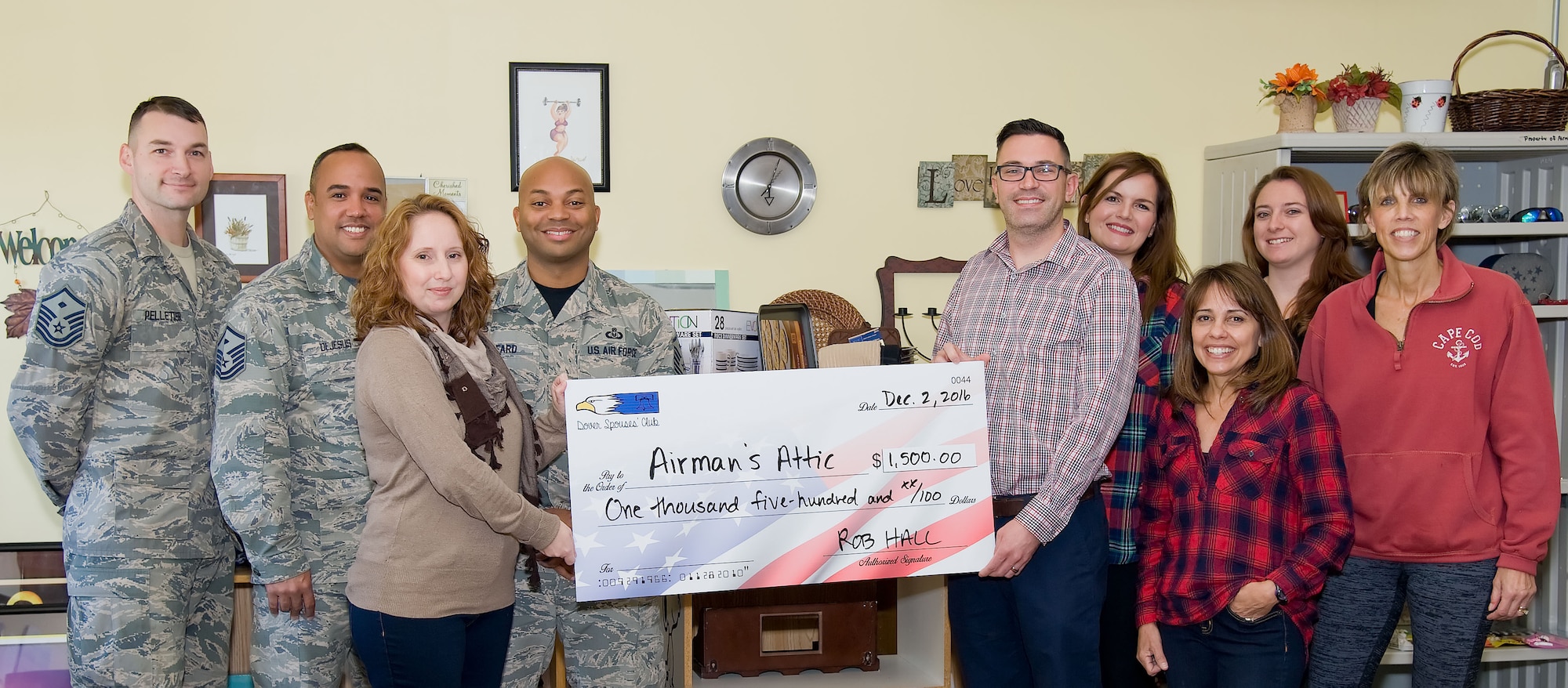 Rob Hall, Dover Spouses’ Club president, presents a check for $1,000 to Michaela Resler, Airman’s Attic volunteer manager, Dec. 2, 2016, at Dover Air Force Base, Del. The check will be used to purchase items for Airmen home starter kits containing items such as dishes, pots and pans, silverware and bakeware. Pictured are Master Sgt. Elden Pelletier, 436th Medical Group first sergeant; Master Sgt. Juan DeJesus, 436th Aircraft Maintenance Squadron first sergeant; Resler; Master Sgt. Jamie Beard, 436th Security Forces Squadron first sergeant; Hall; Kendall Gann, DSC social chair; Kathy McNulty, Airman’s Attic volunteer; Zelia Little, DSC secretary; and Linda Ahern, Airman’s Attic volunteer. Home starter kits are given to Airmen transitioning out of the dormitories into the local community. (U.S. Air Force photo by Roland Balik)