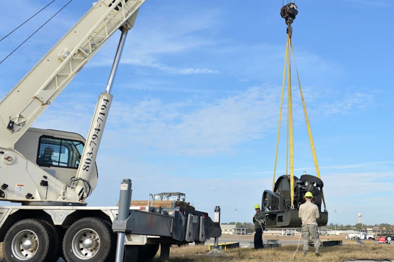 U.S. Airmen assigned to the 20th Civil Engineer Squadron guide a Barrier Artillery Kit-12 rotary friction brake aircraft arresting system as a crane lifts it at Shaw Air Force Base, S.C., Dec. 3, 2016. Airmen and contractors assigned to the 20th CES power production flight performed the replacement so the systems could be ready for inspection the following week. (U.S. Air Force photo by Airman 1st Class Christopher Maldonado)