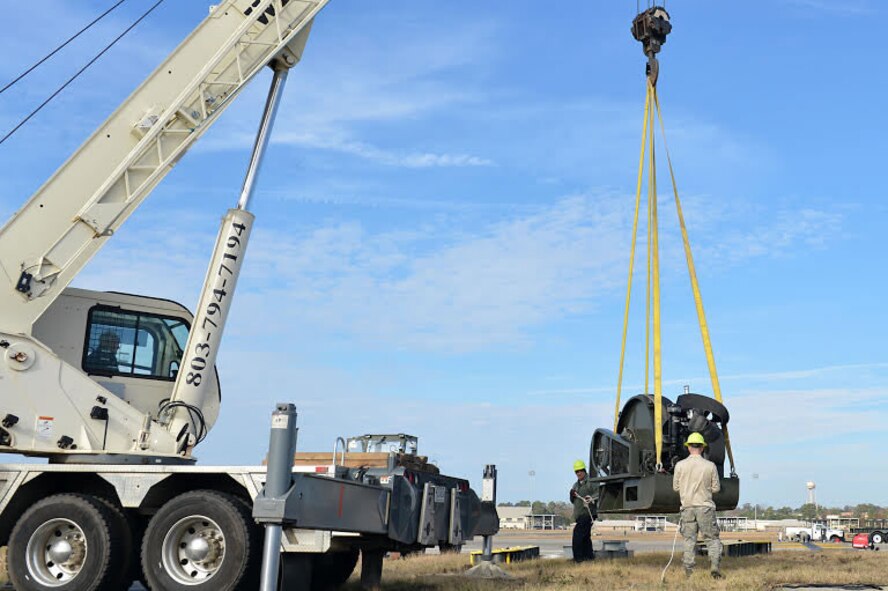 U.S. Airmen assigned to the 20th Civil Engineer Squadron guide a Barrier Artillery Kit-12 rotary friction brake aircraft arresting system as a crane lifts it at Shaw Air Force Base, S.C., Dec. 3, 2016. Airmen and contractors assigned to the 20th CES power production flight performed the replacement so the systems could be ready for inspection the following week. (U.S. Air Force photo by Airman 1st Class Christopher Maldonado)