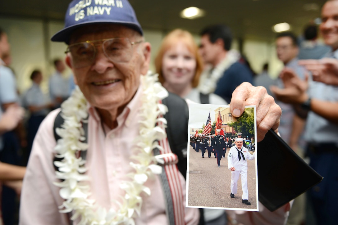 A Navy World War II veteran shows a photograph of himself in uniform after his arrival from Los Angeles at the Honolulu International Airport, Dec. 3, 2016. Coast Guard photo by Petty Officer 2nd Class Tara Molle