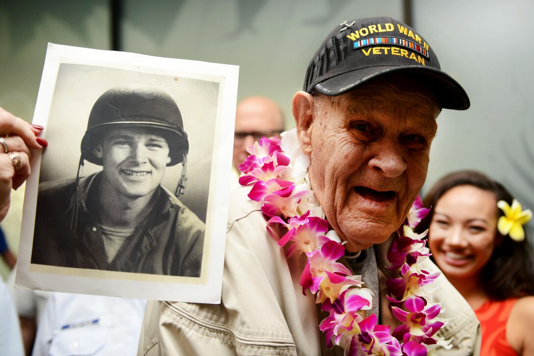A World War II veteran holds an old photograph of himself while being greeted by service members after his arrival from Los Angeles at the Honolulu International Airport, Dec. 3, 2016. Coast Guard photo by Petty Officer 2nd Class Tara Molle