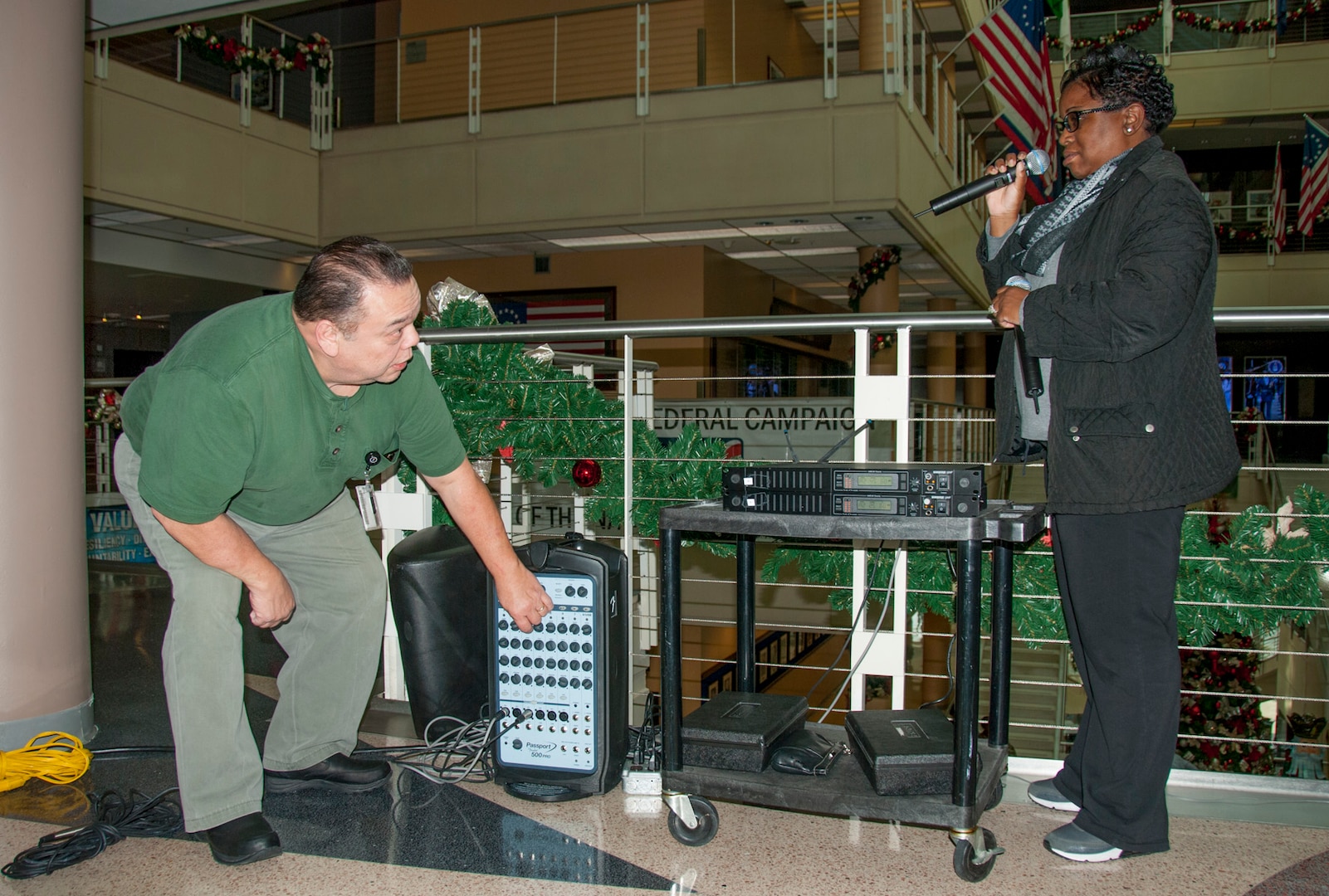 Multimedia specialists Vincent Mundo (left) and Devetrias Johnson (right) set up a sound system so employees hugging the rails on all five floors of the McNamara Headquarters Complex can hear the music and guest speakers during the annual HQC tree lighting ceremony Dec. 7. 