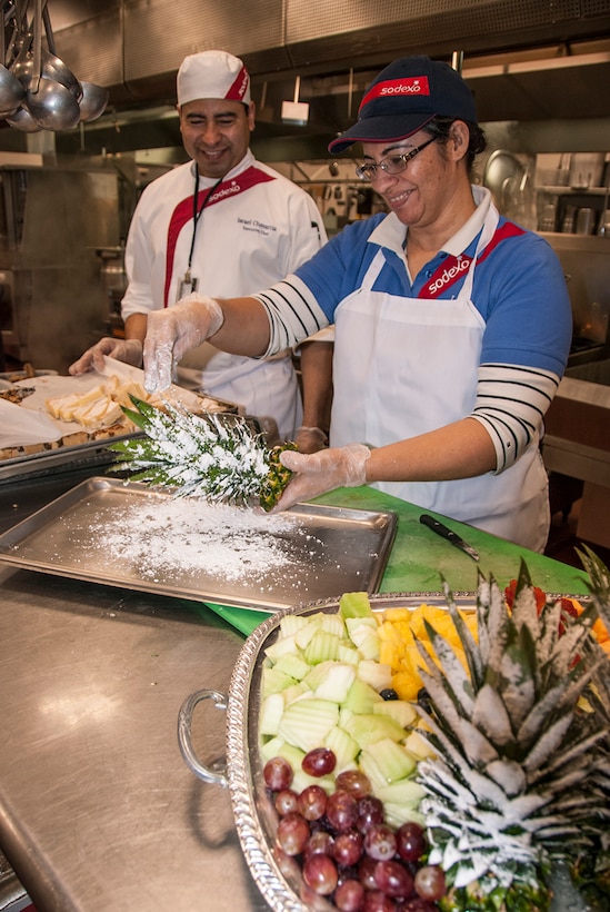 Lety Flores (right) sprinkles powdered sugar over a pineapple top for a snowy effect as Israel Chavarria (left) watches at the McNamara Headquarters Complex Dec. 7. Her creation will serve as a garnish on complementary fruit and cookies trays available during a holiday social following the annual HQC tree lighting ceremony.

