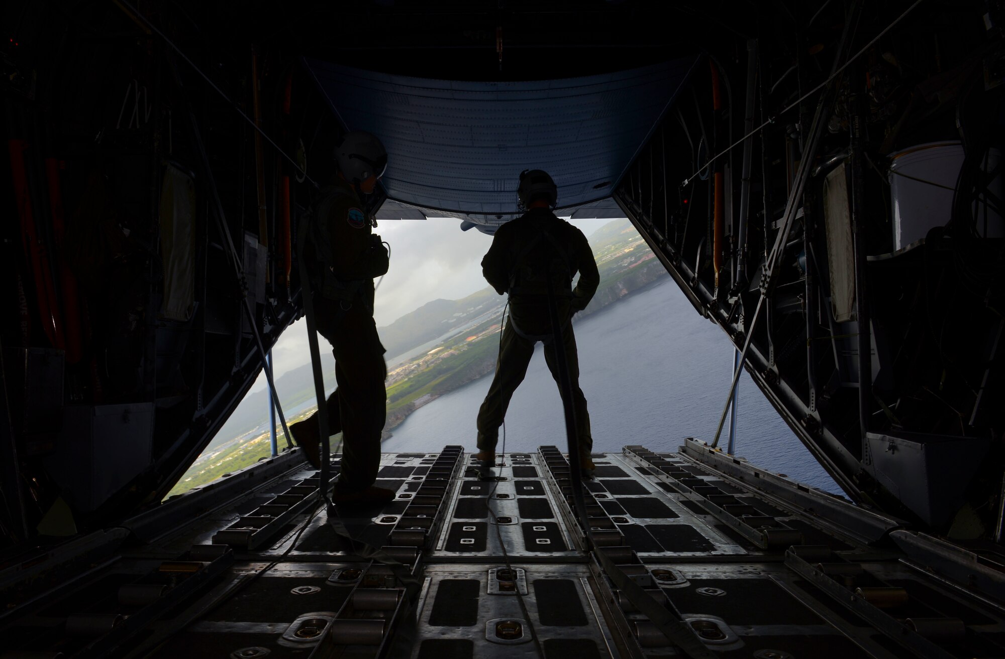 Staff Sgt. Timothy Johnson, right, and Senior Airman Anthony Schoof, 36th Airlift Squadron loadmasters, look out of the back of a C-130 H after releasing a practice bundle over the Micronesian Islands Dec. 5, 2016. The practice bundle drop was part of Operation Christmas Drop, a joint-training operation between the U.S. Air Force, the Royal Australian Air Force, and the Japanese Air Self Defense Force which delivers bundles of donated supplies to the Micronesian Islands. This year is the 65th anniversary of OCD, making it the longest running humanitarian mission in the world. (U.S. Air Force photo by Senior Airman Elizabeth Baker/Released)