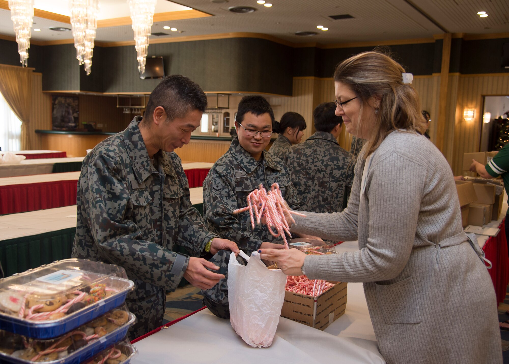 Japan Air-Self Defense Force members receive candy canes from Karri Frizzell, the Cookie Caper committee leader, during the annual event at Misawa Air Base, Japan, Dec. 7, 2016. The Cookie Caper leads also included JASDF members because they are also away from their families during the holidays. Additionally, the volunteers provided a CD of holiday music as an extra gift to the JASDF members. (U.S. Air Force photo by Senior Airman Deana Heitzman)