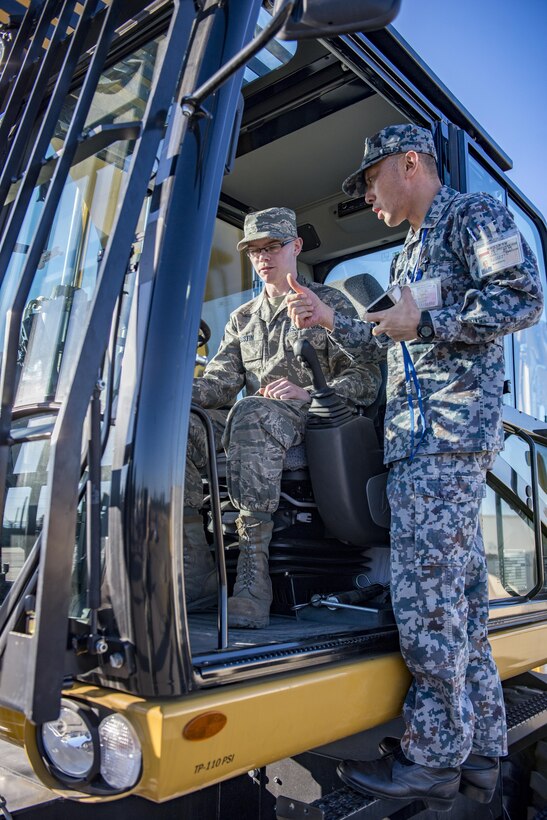U.S. Air Force Airman 1st Class Bradley C. Gustin, 374th Civil Engineering Squadron pavement and construction equipment apprentice, shows a Japan Air Self Defense Force member how to operate new equipment during a Rapid Airfield Damage Repair demonstration Dec. 6, 2016, at Yokota Air Base, Japan. The purpose of the RADR demonstration is to share capabilities and techniques with JASDF members in the event of an airfield attack and to promote bilateral engagement between the U.S. and Japan. (U.S. Air Force photo by Airman 1st Class Donald Hudson/Released)
