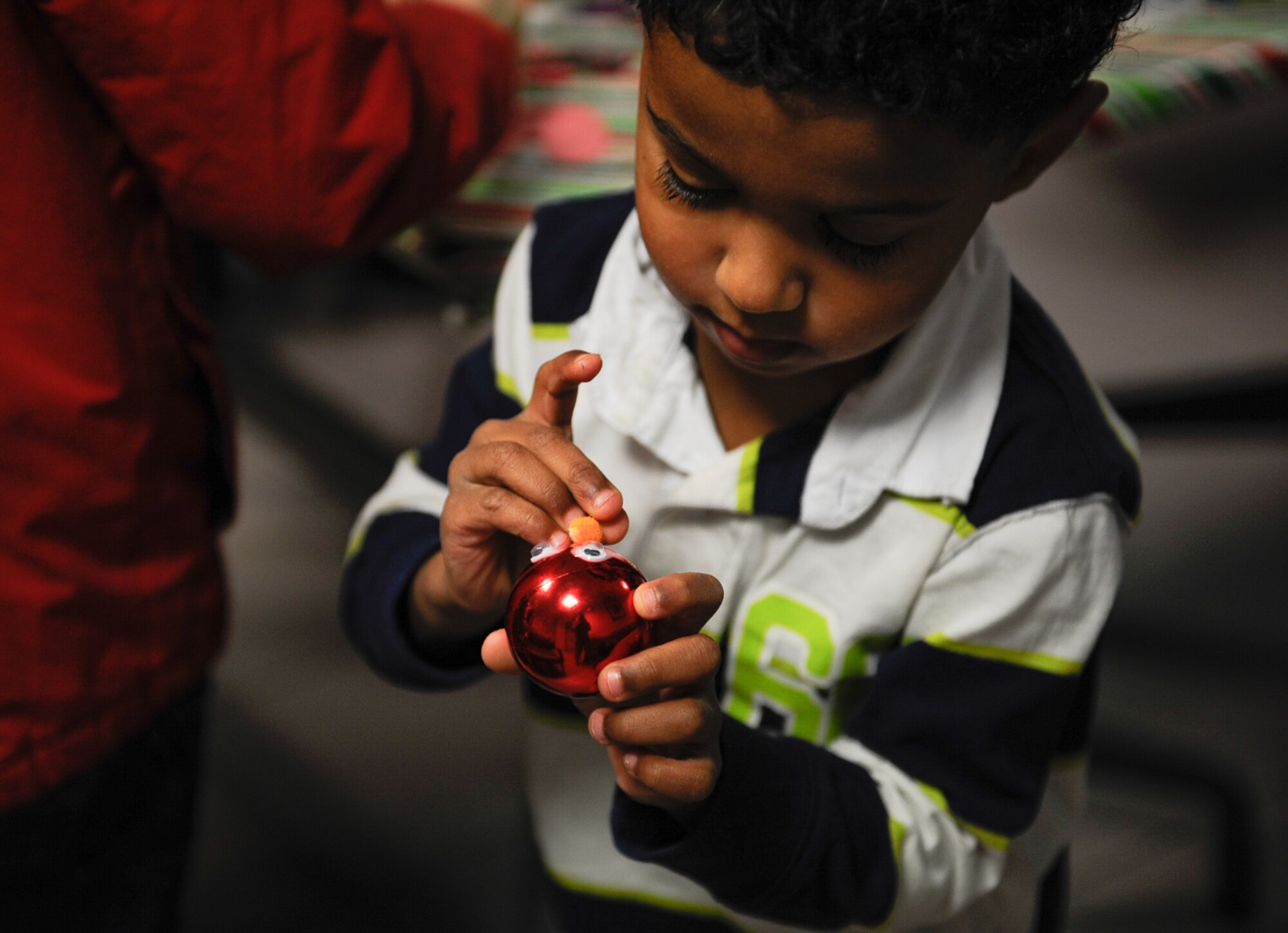 Khalil Mackey, son of Tech. Sgt. Corey Mackey, 786th Force Support Squadron glues an orange nose to his Christmas ornament at Ramstein Air Base, Germany, Dec. 1, 2016. Khalil and his parents attended  the 86th Medical Group Christmas tree lighting ceremony, participated in crafts, a Christmas card reveal, sipped warm beverages alongside other attendees and watched the Christmas tree come to life. (U.S. Air Force photo/Airman 1st Class Savannah L. Waters)