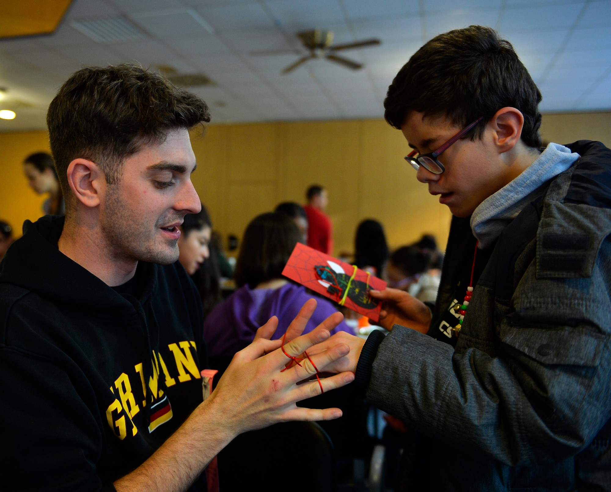 Airman James Coolbaugh, 86th Munitions Squadron tactical aircrew rapid response packages crewmember, demonstrates a trick using string to a German student during the 2016 Winter Special Olympics at Vogelweh Military Complex, Germany, Dec. 2. The event was designed to give special needs children, both Americans and Germans, a chance to participate in modified sports. (U.S. Air Force photo by Airman 1st Class Joshua Magbanua)
