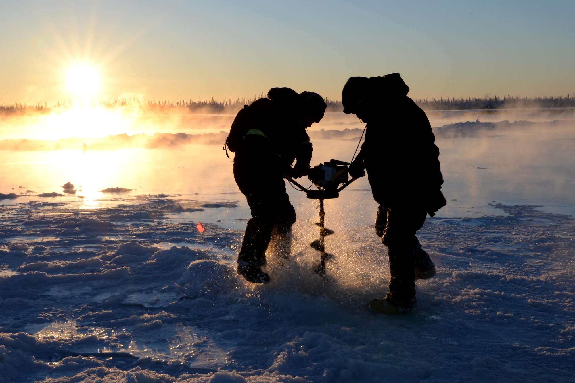 U.S. Air Force Senior Airman Carlos Aleman, a 354th Civil Engineer Squadron range maintenance technician, uses an auger to drill a hole in the frozen Tanana River with Tech. Sgt. Craig Slaten, the 354th CES noncommissioned officer in charge of service contracts, Dec. 5, 2016, in Fairbanks, Alaska. Slaten and Aleman use the auger to drill into the ice, exposing water which will build up the ice and create a stable bridge for transportation of equipment and supplies. (U.S. Air Force photo by Airman 1st Class Cassandra Whitman)