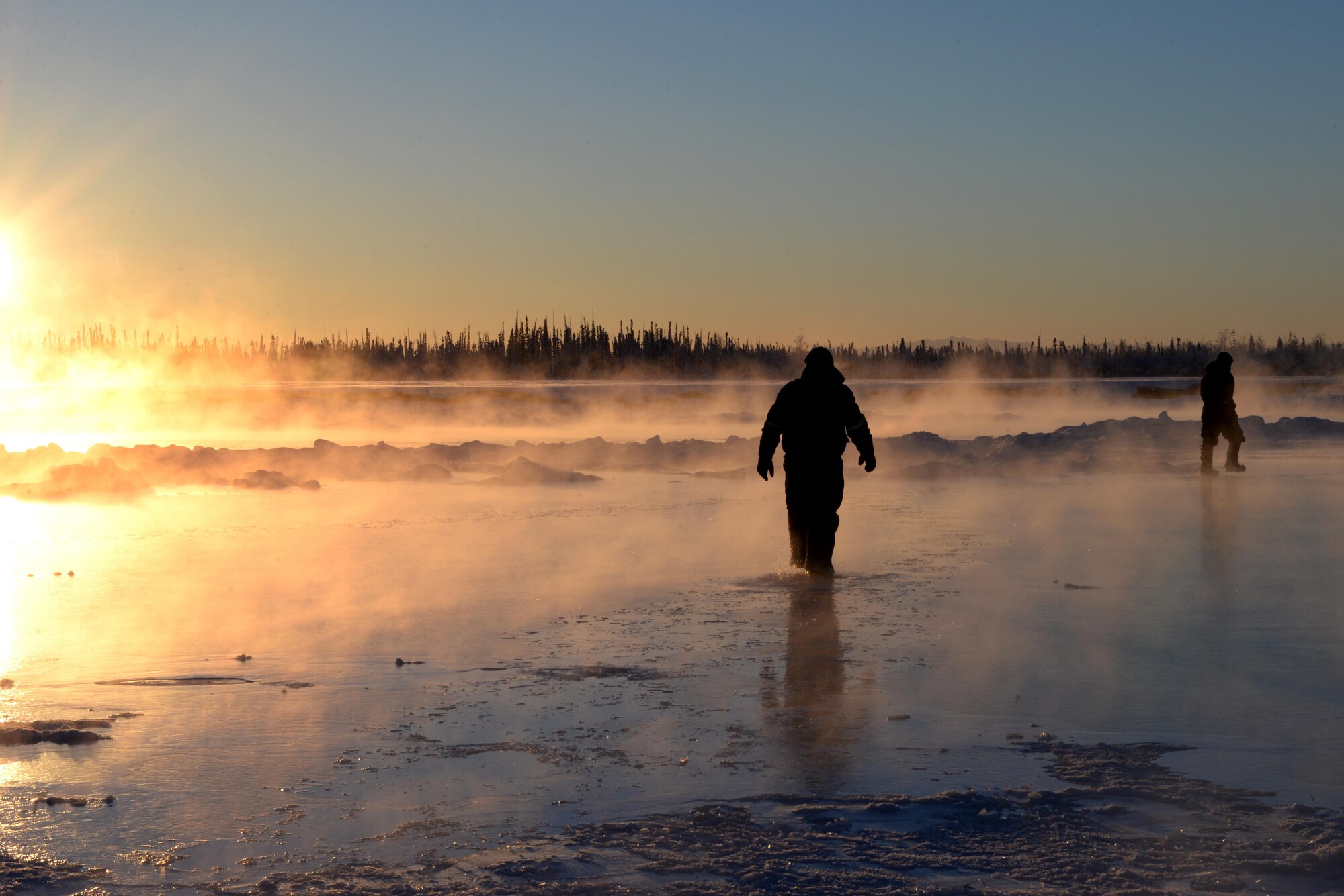 U.S. Air Force Senior Airman Carlos Aleman, a 354th Civil Engineer Squadron range maintenance technician, walks through water as it freezes over existing ice on the Tanana River with Tech. Sgt. Craig Slaten, the 354th CES noncommissioned officer in charge of service contracts, Dec. 5, 2016, in Fairbanks, Alaska. A team of Airmen build up the ice bridge every two years to make transportation of equipment and materials easier for the Airmen and civilians who work at the Blair Lakes Range Maintenance Complex. (U.S. Air Force photo by Airman 1st Class Cassandra Whitman)