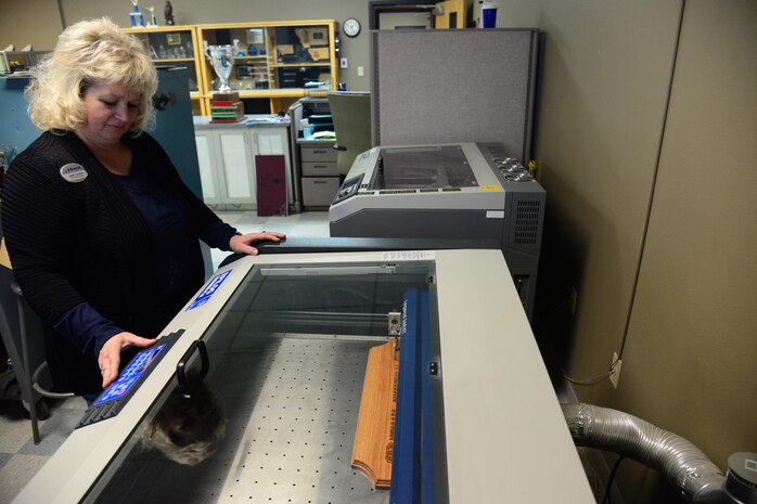 Sherry Pschernig, 341st Force Support Squadron’s Arts and Crafts Center engraver, creates a wooden plaque Dec. 7, 2016, at Malmstrom Air Force Base, Mont. The Engraving Shop has the capability to make wooden plaques from scratch by utilizing a machine that can burn personalized designs and words into the wood. (U.S. Air Force photo/Airman 1st Class Magen M. Reeves)	