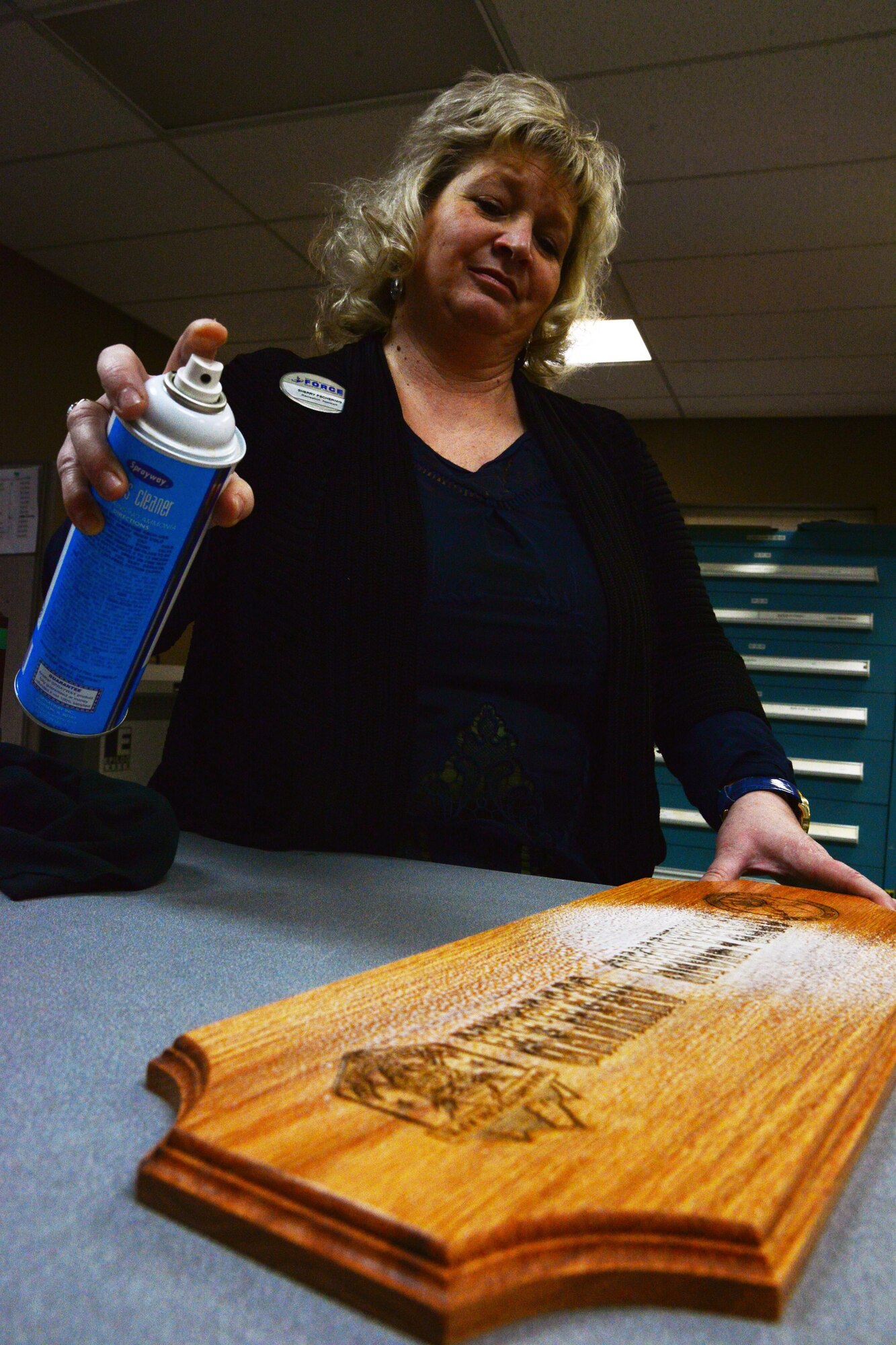Sherry Pschernig, 341st Force Support Squadron Arts and Crafts Center engraver, sprays a wooden plaque Dec. 7, 2016, at Malmstrom Air Force Base, Mont. The Engraving Shop has the capability to make wooden plaques from scratch, which then have to be polished and treated for longevity to ensure the best quality product possible for the customer. (U.S. Air Force photo/Airman 1st Class Magen M. Reeves)	