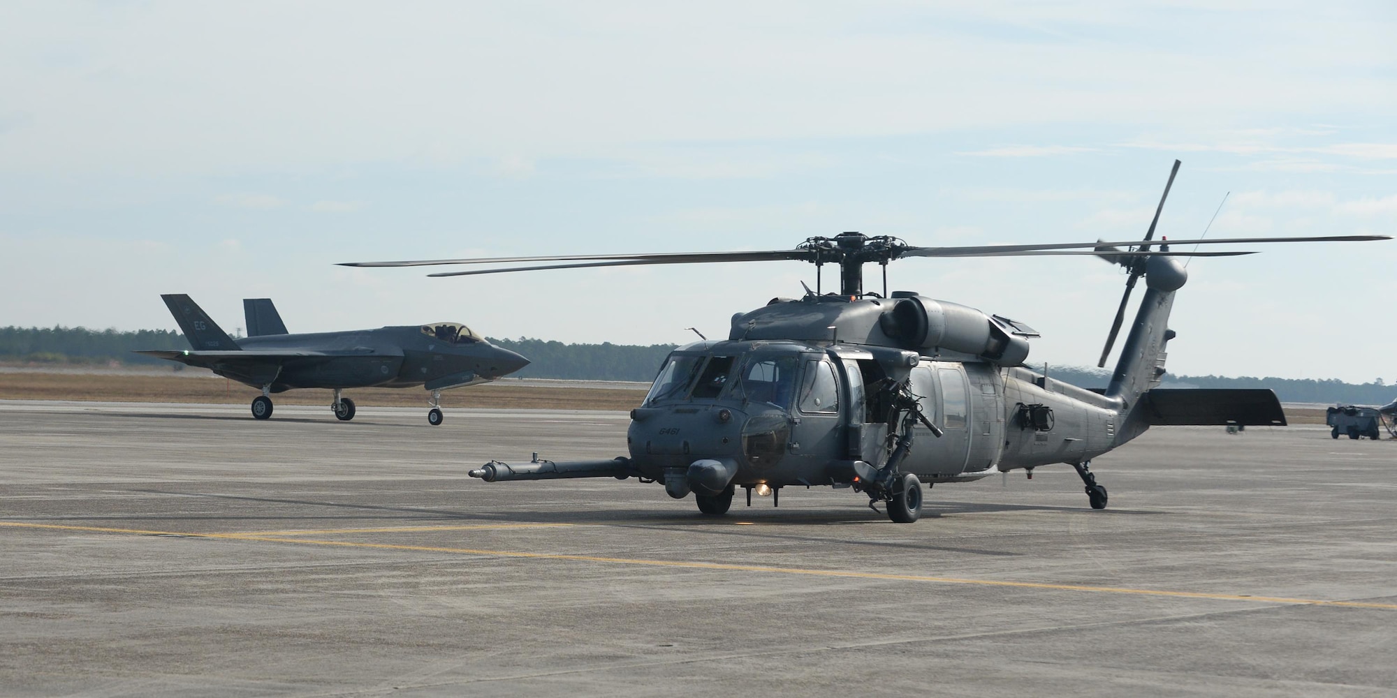 A U.S. Air Force 66th Rescue Squadron HH-60G Pave Hawk waits to takeoff as an F-35 Lightning II taxies down the runway at Tyndall Air Force Base, Fla., Dec. 8, 2016. Pave Hawks from the 66th RQS, Nellis Air Force Base, Nevada, came to Tyndall for Checkered Flag 17-1. (U.S. Air Force photo by Airman 1st Class Cody R. Miller/Released)