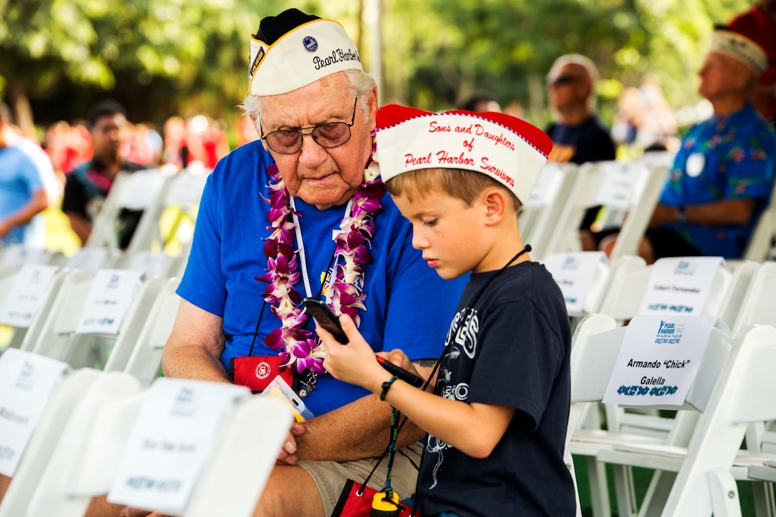 A child teaches Pearl Harbor survivor Lester “Les” Lindow how to use modern technology during the Pearl Harbor Memorial Parade at Fort Derussy Beach Park, Hawaii, Dec. 7, 2016. Lester was stationed aboard the USS Maryland during the attack on Pearl Harbor. Marine Corps photo by Lance Cpl. Robert Sweet