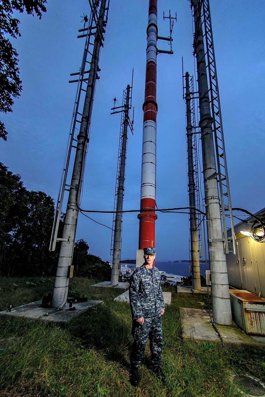 Petty Officer 2nd Class Brandon Armstrong, a meteorological forecaster, stands under the Automated Surface Observing System (ASOS) on Yokosuka Naval Base.