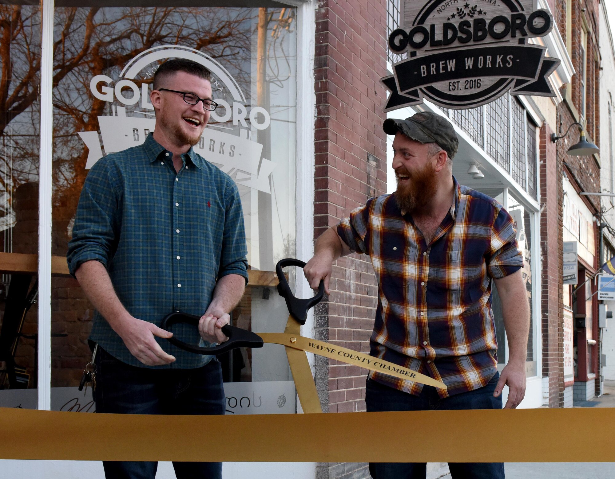 U.S. Air Force veterans Carson Clark (left) and Zac Fein (right) cut a ribbon for the grand opening of their, Dec. 2, 2016, in Downtown Goldsboro, North Carolina. Fein and Clark both finished their enlistment at Seymour Johnson Air Force Base, North Carolina as F-15E Strike Eagle crew chiefs assigned to the 4th Aircraft Maintenance Squadron. (U.S. Air Force photo by Airman Miranda A. Loera)