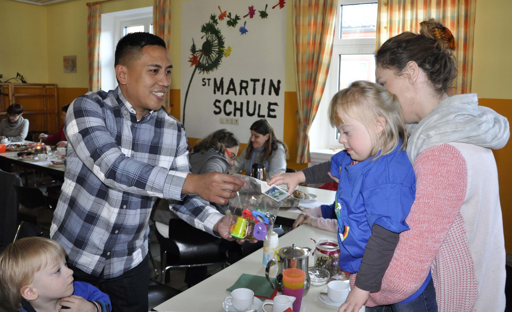 A member of the 52nd Civil Engineer Squadron hands out a gift to a child at the Bitburg Saint Martin school, Dec. 5, during the school’s annual Sankt Nicholas celebration. The event included a visit by Sankt Nicholas, dances and singing performances by the children, as well as a gift presentation by the 52nd Fighter Wing. The celebration was attended by Saint Martin school officials, parents, 52nd Fighter Wing leadership spouses, as well as Airmen and civilians from the wing, who provided gifts to students and kindergarten children.  In the summer, Spangdahlem Sabers invited the Saint Martin school to Special Children’s Day at Spangdahlem AB, where they played games and spent a fun-filled time together. (U.S. Air Force photo by Iris Reiff)