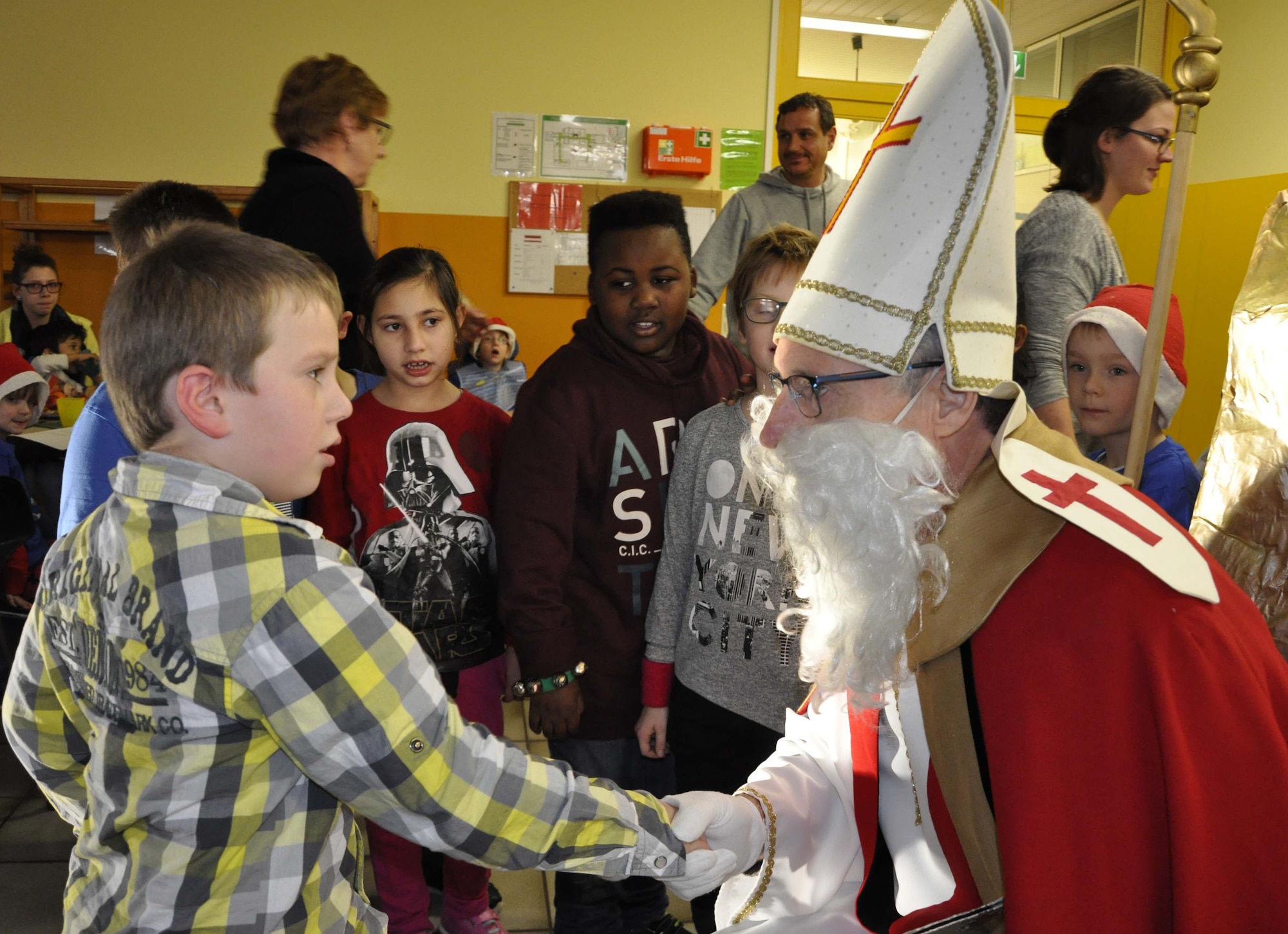 A school student of the Bitburg Saint Martin school shakes hands with Sankt Nicholas during the school's annual Saint Nicholas celebration, Dec. 5 in Bitburg. The event included a visit by Saint Nicholas, dances and singing performances by the children, as well as a gift presentation by the 52nd Fighter Wing. The celebration was attended by Saint Martin school officials, parents, 52nd Fighter Wing leadership spouses, as well as Airmen and civilians from the wing, who provided gifts to students and kindergarten children. In the summer, Spangdahlem Sabers invited the Saint Martin school to Special Children’s Day at Spangdahlem AB, where they played games and spent a fun-filled time together. (U.S. Air Force photo by Iris Reiff)