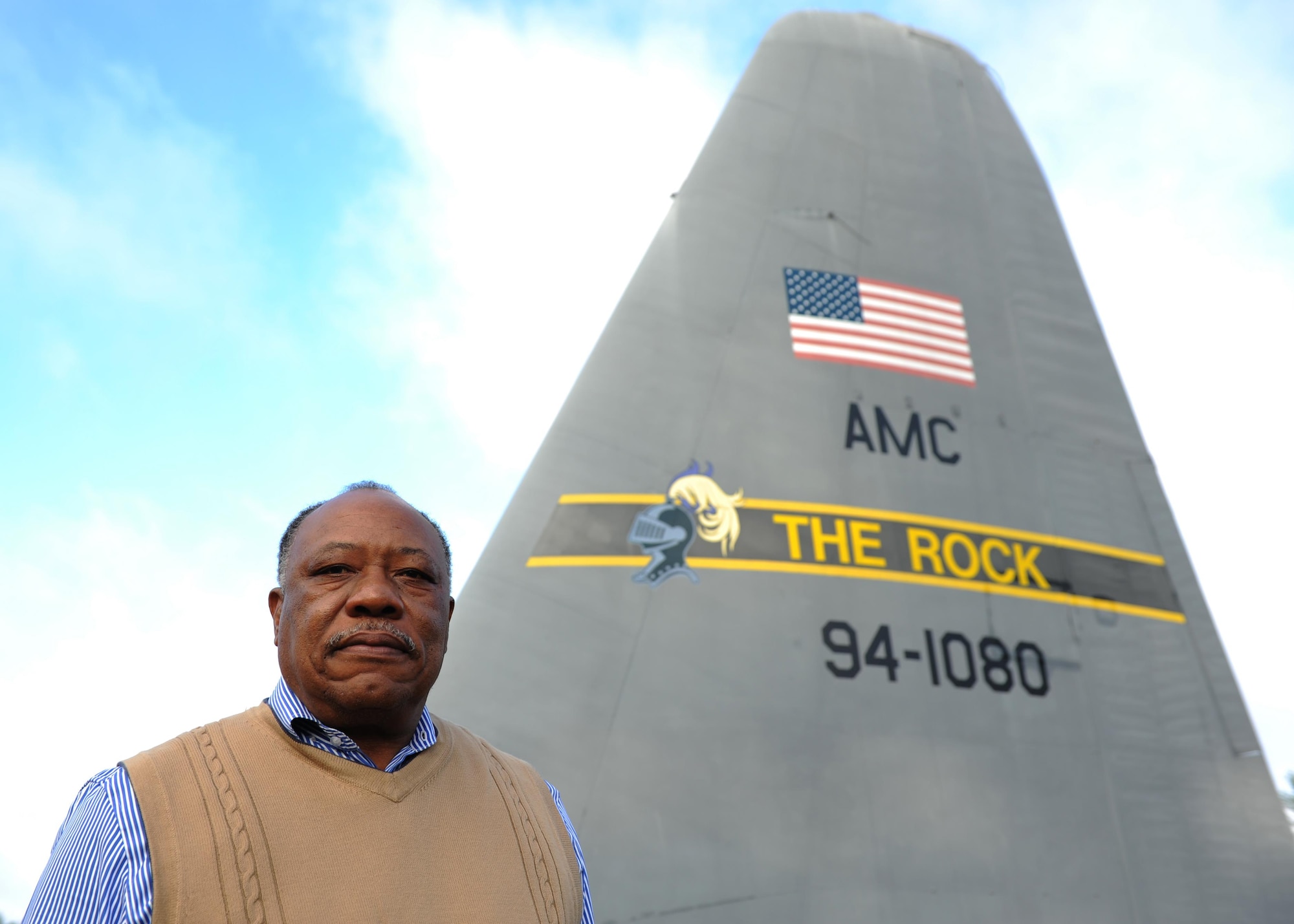 Retired U.S. Air Force Chief Master Sgt. Willie Goodwin, 19th Maintenance Group Engineering and technical services specialist, stands in front of the old tail of the last C-130E to leave Little Rock Air Force Base. The tail was removed from the C-130E and repainted to serve as a landmark in front of Hangar 1080. (U.S. Air Force photo by Airman 1st Class Grace Nichols)