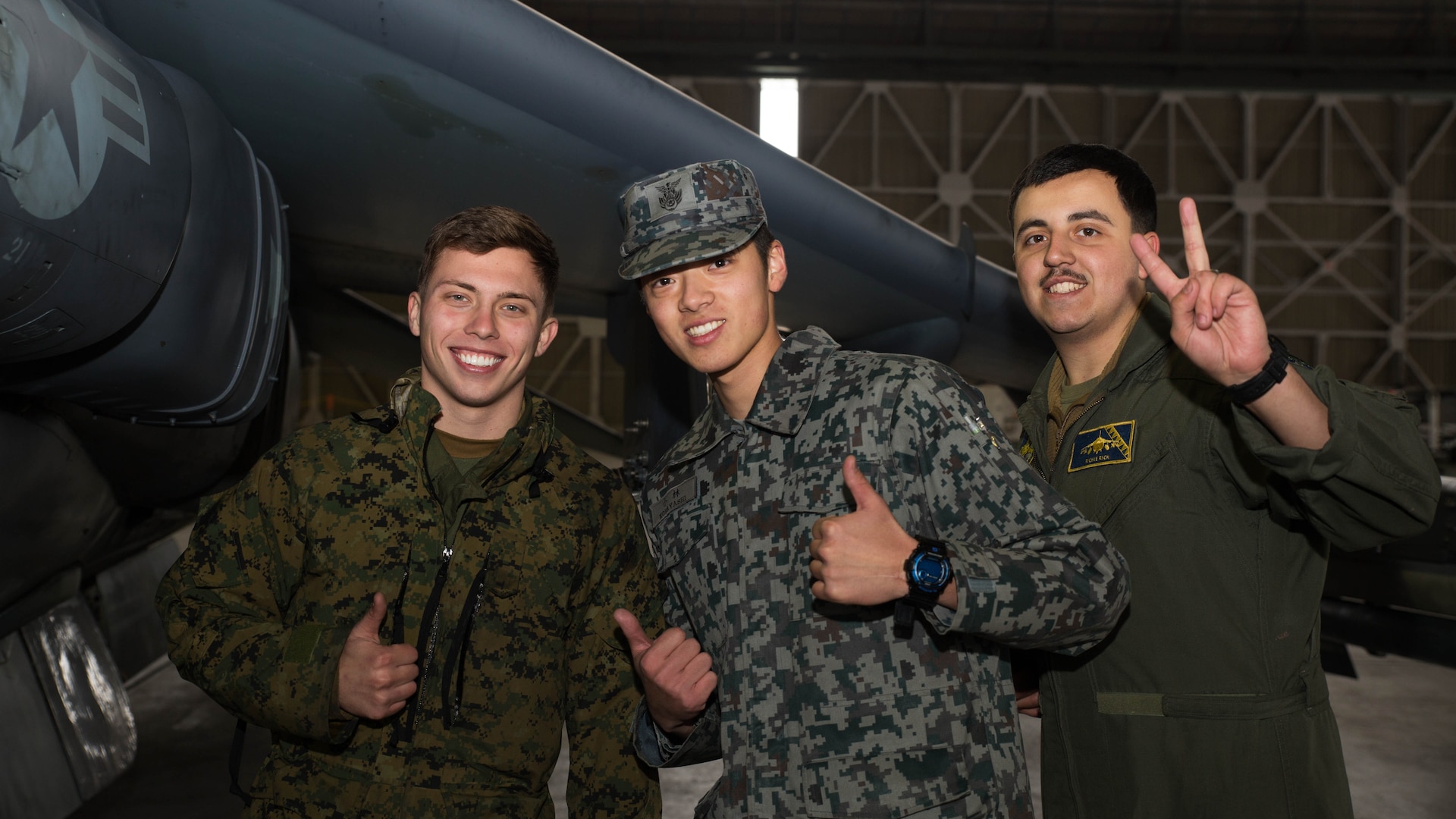 U.S. Marine Corps Lance Cpls. Austin Nazworth, left, and Breht Urzua, right, power line technicians with Marine Attack Squadron (VMA) 542, pose for a photo with a member of the Japan Air Self Defense Force at Chitose Air Base, Japan, Dec. 9, 2016. JASDF personnel joined the VMA-542 Marines in their hangar to get a closer look and better understanding of the squadrons Harriers. (U.S. Marine Corps photo by Lance Cpl. Joseph Abrego)