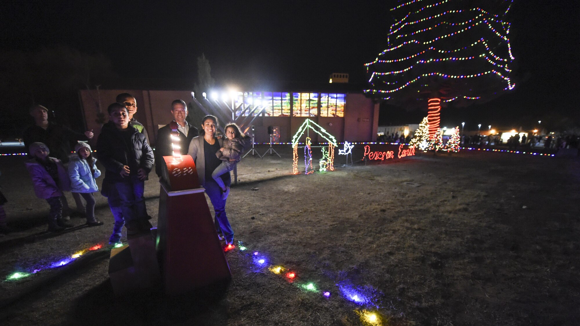 Col. Houston Cantwell, the 49th Wing commander along with Vanessa Bordelon, wife of deployed member from the 2nd Lt. Dustin Bordelon, 49th Aircraft Maintenance Squadron and their two sons stand next to decorative holiday lights during the base menorah and tree lighting ceremony Dec. 7, at the base chapel. Santa made an appearance on a fire truck and children sang holiday-themed songs during the ceremony. (U.S. Air Force photo by Staff Sgt. Stacy Jonsgaard)