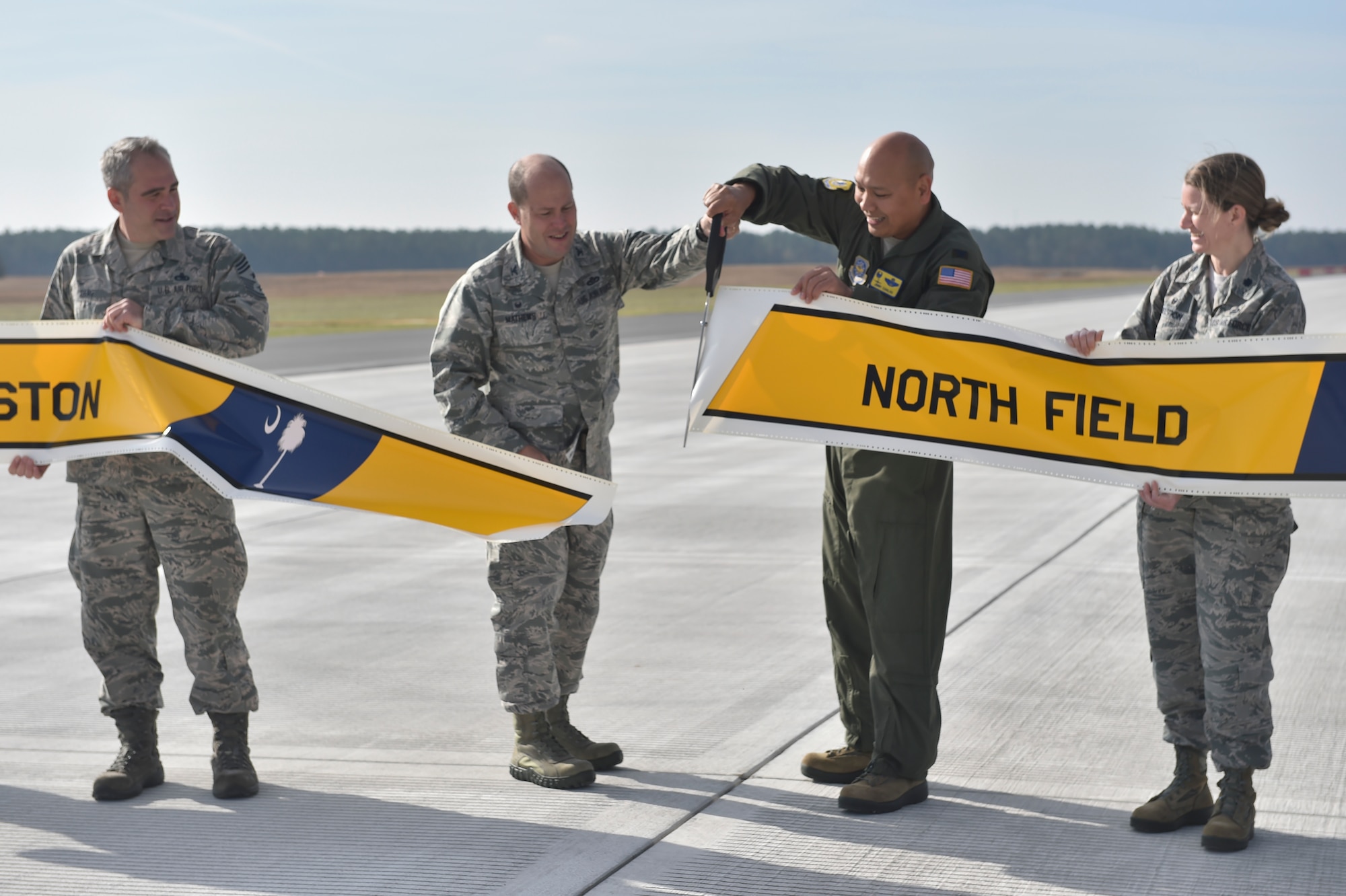 U.S. Air Force Col. Jimmy Canlas 437 Airlift Wing commander, middle right and U.S. Air Force Col. Richard Mathews, 628th Mission Support Group commander, middle left, cut a banner marking the completion of repairs to the North Auxiliary Airfield Runway in North, South Carolina, Dec. 8, 2016. Repairs included approximately 21,000 tons of asphalt repurposed as the foundation below the new concrete, 66,000 linear feet of wire, a new runway lighting system and an additional 36,000 square yards of asphalt shoulder to the landing zone.