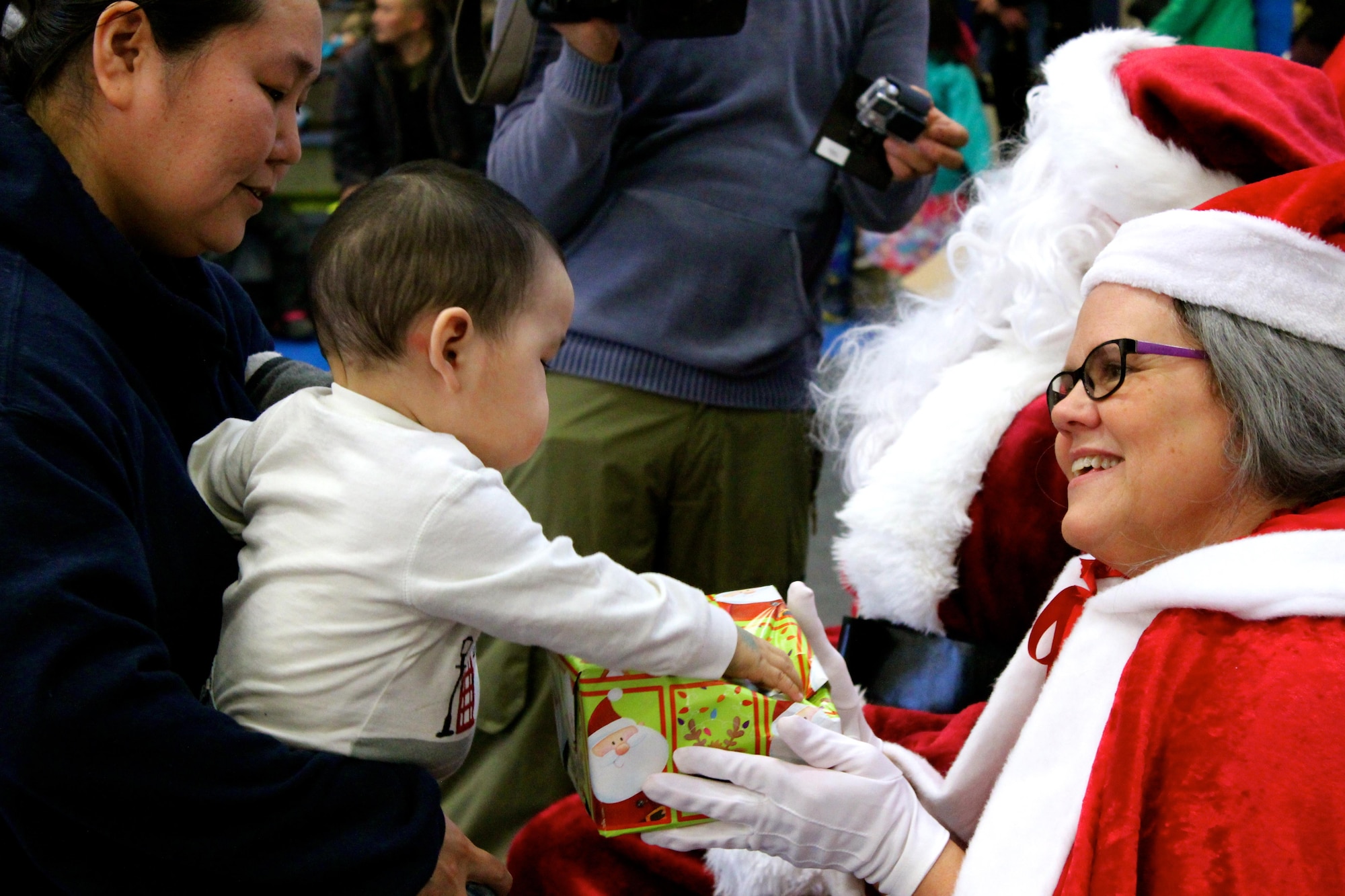 Mrs. Claus hands a gift to a young Akiachak child during Operation Santa Claus, Dec. 3, 2016. This year marked the 60th anniversary in which the Alaska National Guard supported Operation Santa Claus with logistics and air support, delivering holiday cheer and gifts to remote Alaska villages. (U.S. Army National Guard photo by Capt. Amanda Plachek)