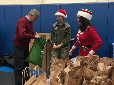 Alaska Lt. Gov. Byron Mallot inspects the contents of a Santa's elf goodie bag as he prepares to hand out gifts with U.S Air Force Airman 1st Class Andrea Yacabell to children in Akiachak Dec. 3, 2016. April Gettys (right) coordinated the Operation Santa Claus mission with the Alaska National Guard, in it's 60th year. (U.S. Air National Guard photo by Lt. Col. Candis Olmstead)