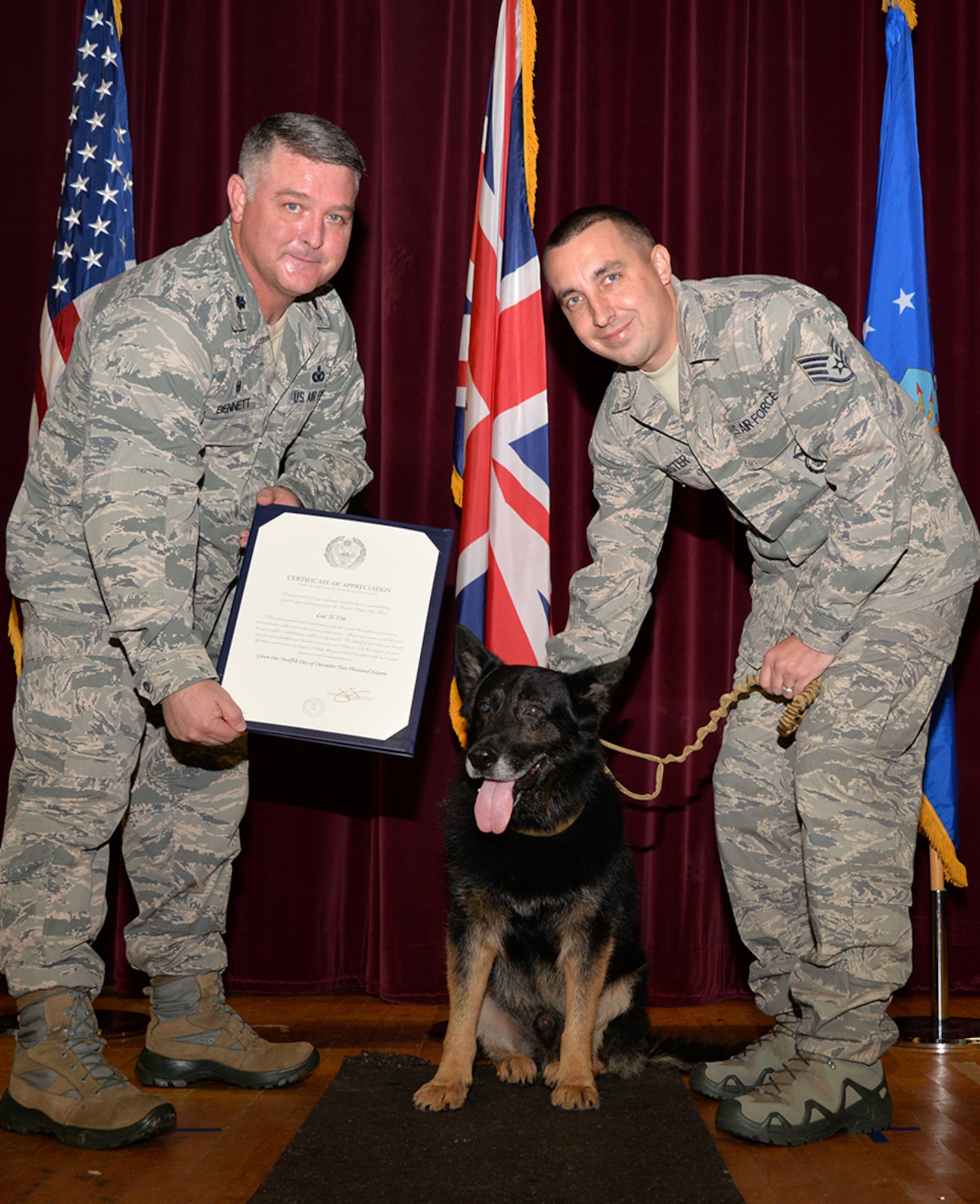 U.S. Air Force Lt. Col. Johnathon Bennett, left, 100th Security Forces commander, presents a Certificate of Appreciation, signed by Chief Master Sergeant of the Air Force, Chief Master Sgt. James Cody, to Military Working Dog Luc as he sits with U.S. Air Force Staff Sgt. Kelly Webster, 100th SFS MWD trainer, during his retirement Dec. 12, 2016, on RAF Mildenhall, England. Luc served seven-and-a-half years – more than 50 “dog years” at RAF Mildenhall, and partnered with five handlers. (U.S. Air Force photo by Karen Abeyasekere)